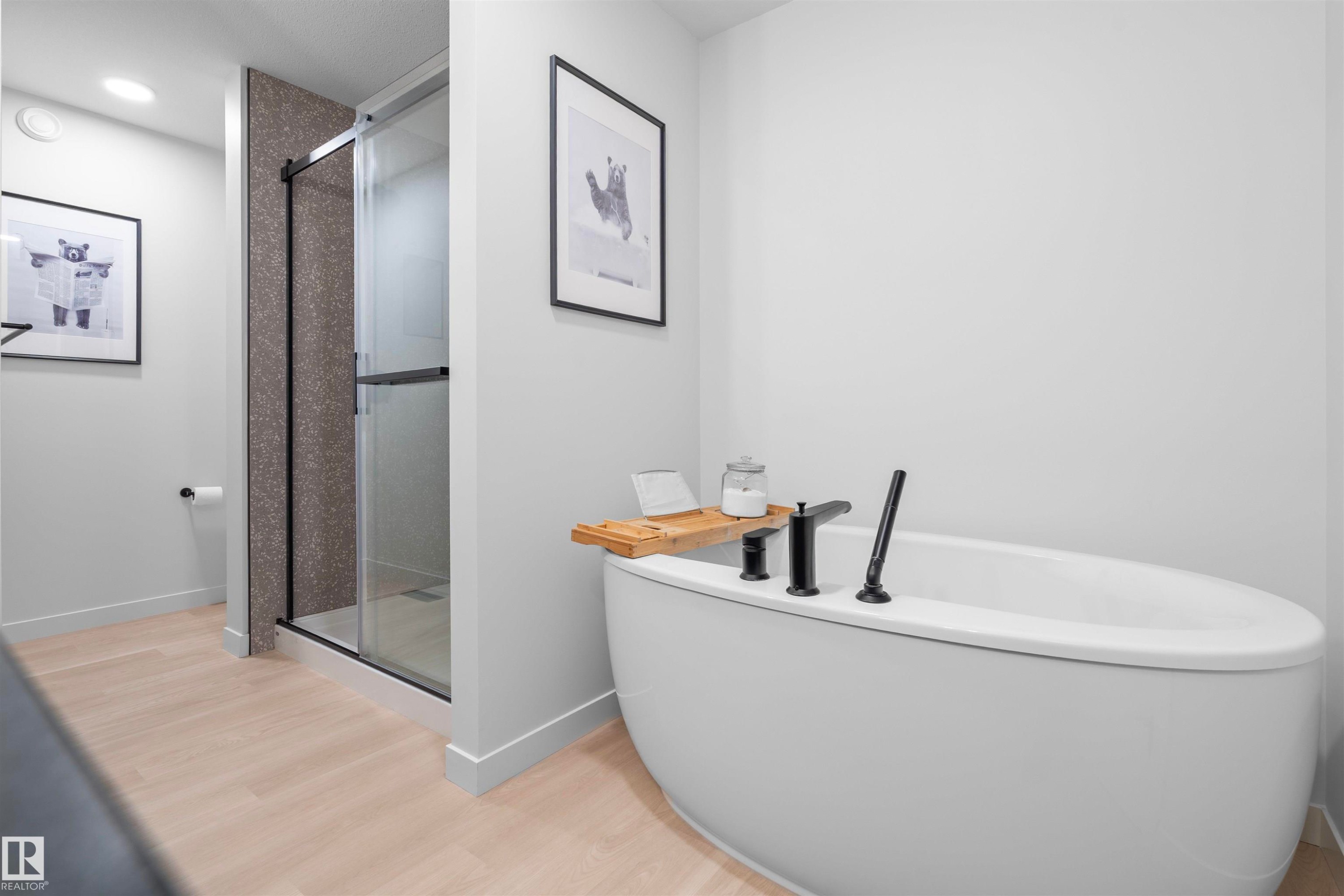 Freestanding soaking tub with black fixtures, walk-in shower with dark-toned tile, and wood-finish flooring - 8047 227 Street Nw, Edmonton, AB