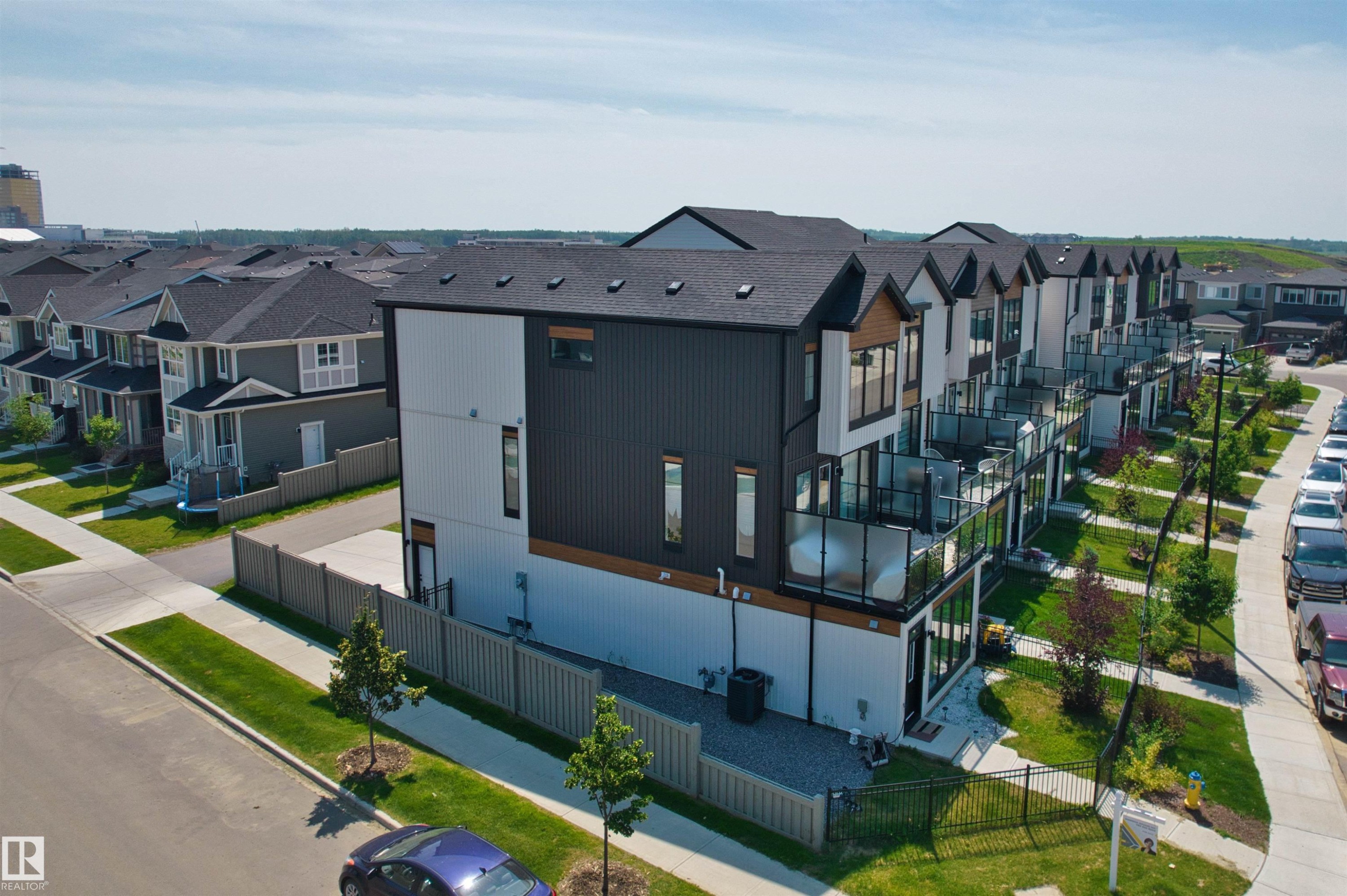 Modern architectural style featuring dark and light panel siding, multiple balconies with glass railings, and a fenced yard with gravel landscaping - 8047 227 Street Nw, Edmonton, AB