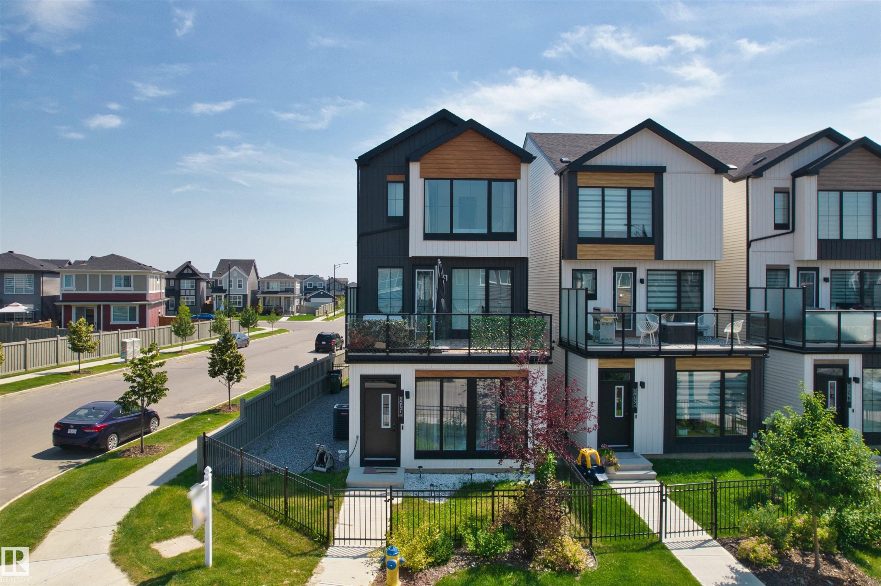 Modern townhome exterior with black frame windows, wood-finish accents, and a ground-level balcony featuring glass railings - 8047 227 Street Nw, Edmonton, AB