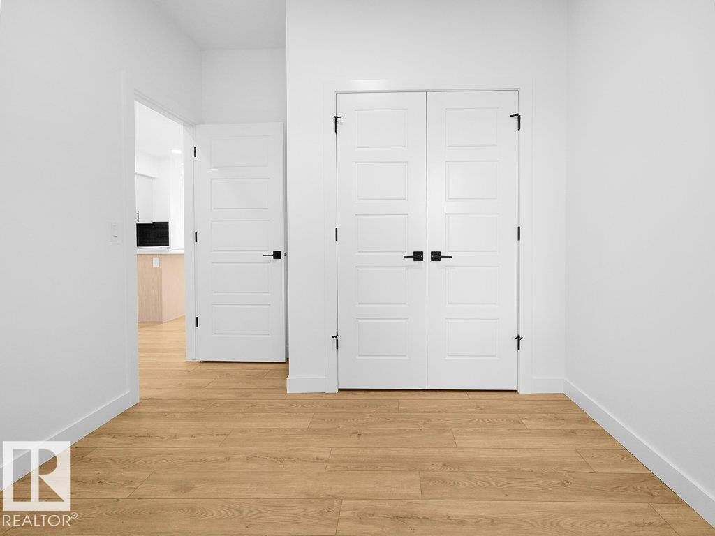 Light wood-finish flooring, white paneled doors, black hardware accents, and bright white walls - 912 17 Ave Nw, Edmonton, AB