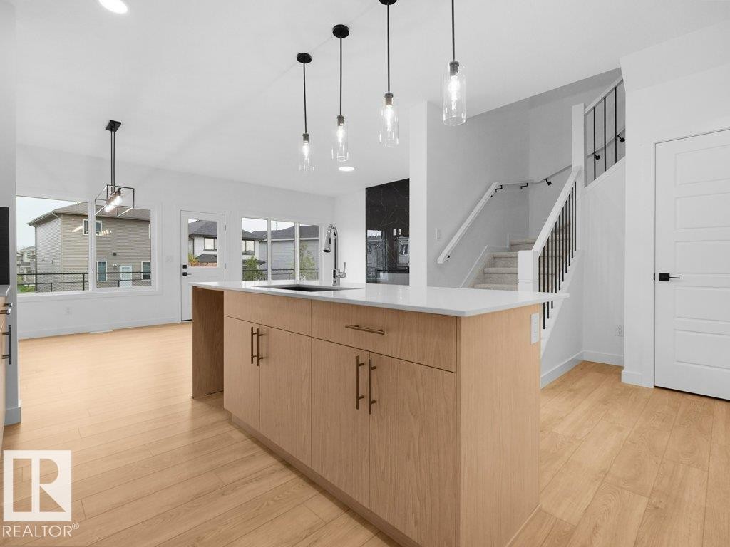 Kitchen island with light wood-finish cabinetry, white countertop, and pendant lighting - 912 17 Ave Nw, Edmonton, AB