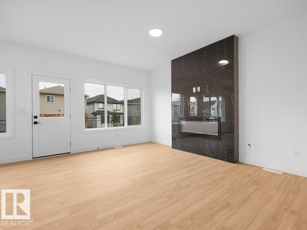 Light wood-finish flooring with an integrated modern fireplace featuring a dark, veined material surround - 912 17 Ave Nw, Edmonton, AB