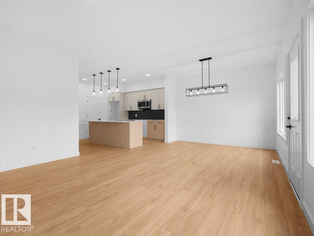 Light wood-finish flooring, white walls, kitchen island with built-in sink, pendant lighting, and a modern rectangular chandelier - 912 17 Ave Nw, Edmonton, AB
