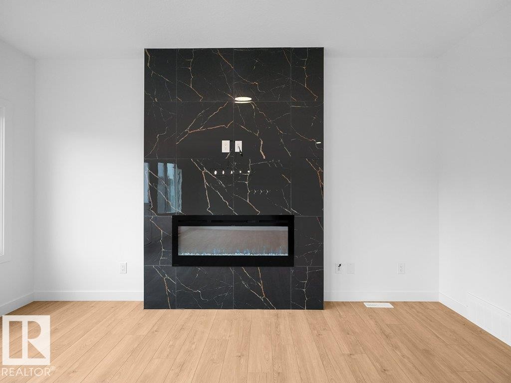 Black tile fireplace surround with gold veining, integrated electric fireplace, and wood-finish flooring - 912 17 Ave Nw, Edmonton, AB