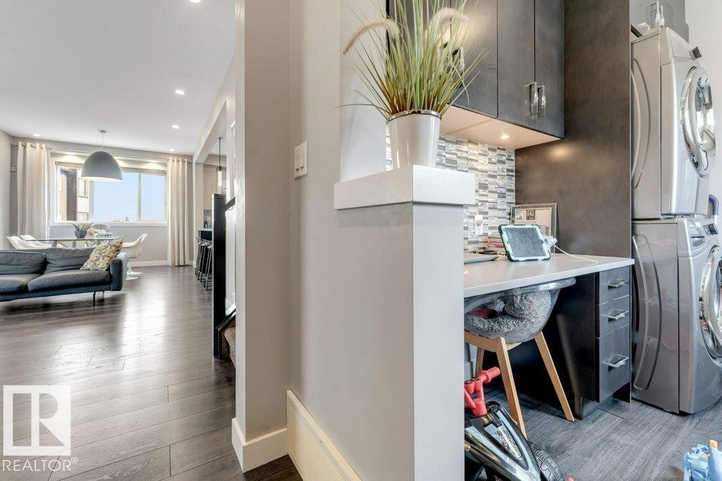 Built-in desk with overhead cabinetry, stacked washer and dryer, mosaic tile backsplash, wood-finish flooring, recessed lighting - #45 16903 68 St Nw, Edmonton, AB