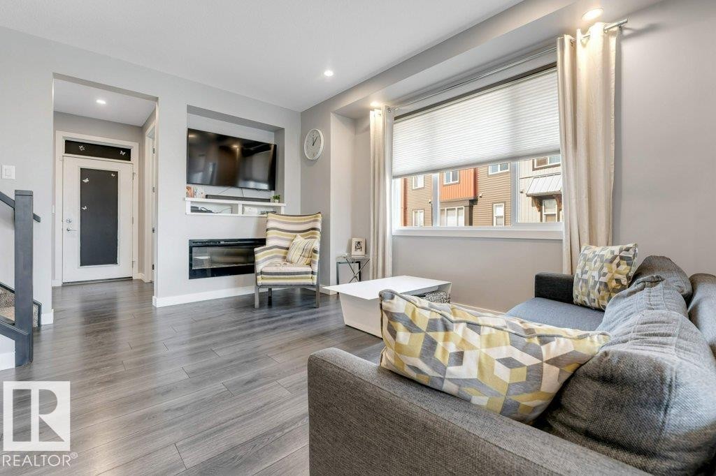 Living area featuring wood-finish flooring, recessed lighting, a built-in media center with shelving, and a large window with blinds - #45 16903 68 St Nw, Edmonton, AB