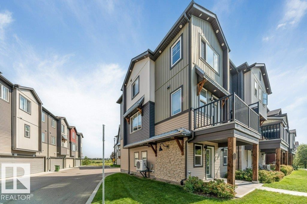 Multi-level townhome featuring a balcony with metal railings, a stone accent wall, and a gabled roofline - #45 16903 68 St Nw, Edmonton, AB