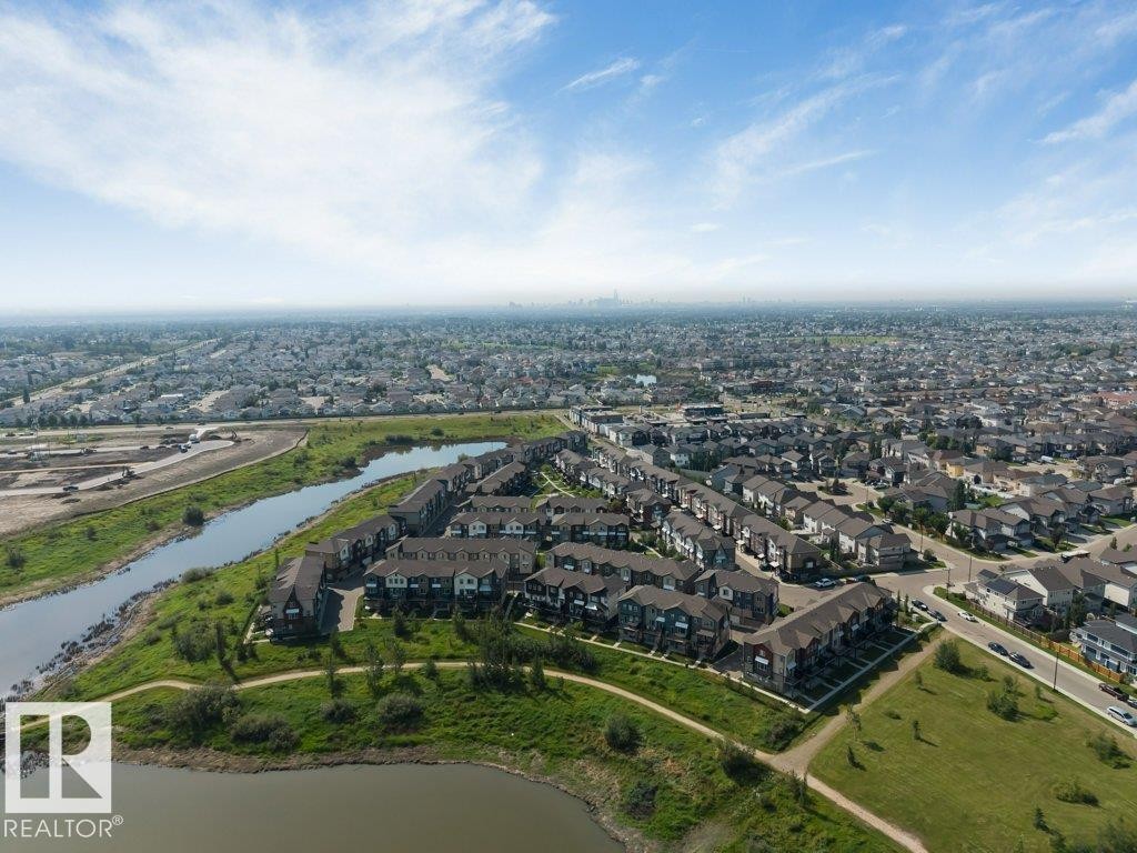 Aerial perspective showcasing a residential development with a waterfront setting, bordered by a paved pathway and green spaces - #45 16903 68 St Nw, Edmonton, AB