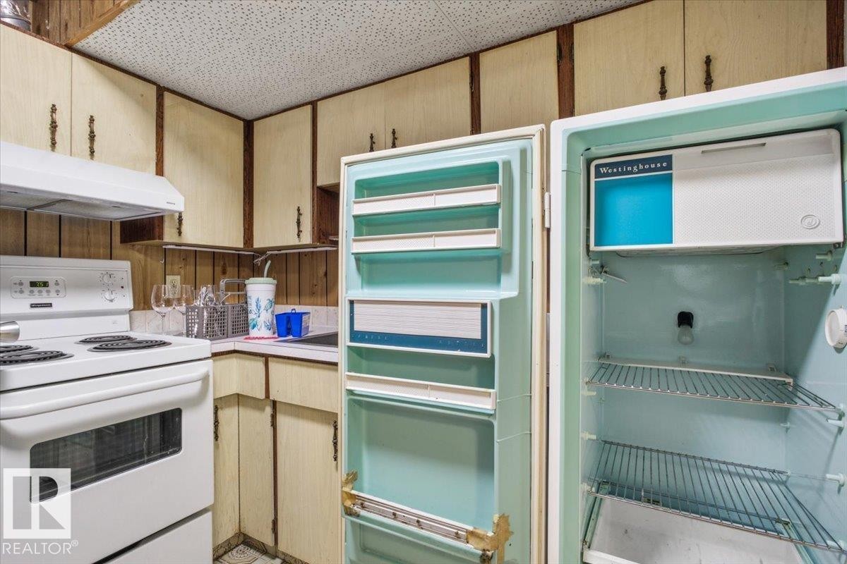 Equipped kitchen with a white electric range, coordinating range hood, and wood-paneled walls - 13235 82 Street Nw, Edmonton, AB