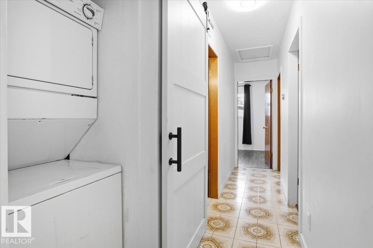Stackable laundry appliances, white panel barn door, matte black hardware, tile flooring with circular patterns, and a flush-mount ceiling light - 13235 82 Street Nw, Edmonton, AB