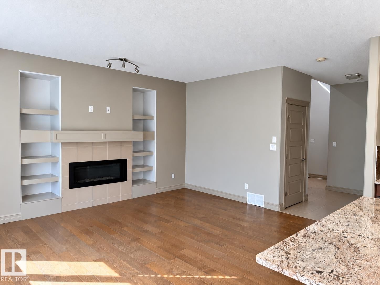 Wood-finish flooring, built-in shelving, tile-surround fireplace, track lighting, and a stone-finish countertop - 885 Windermere Wynd Nw, Edmonton, AB