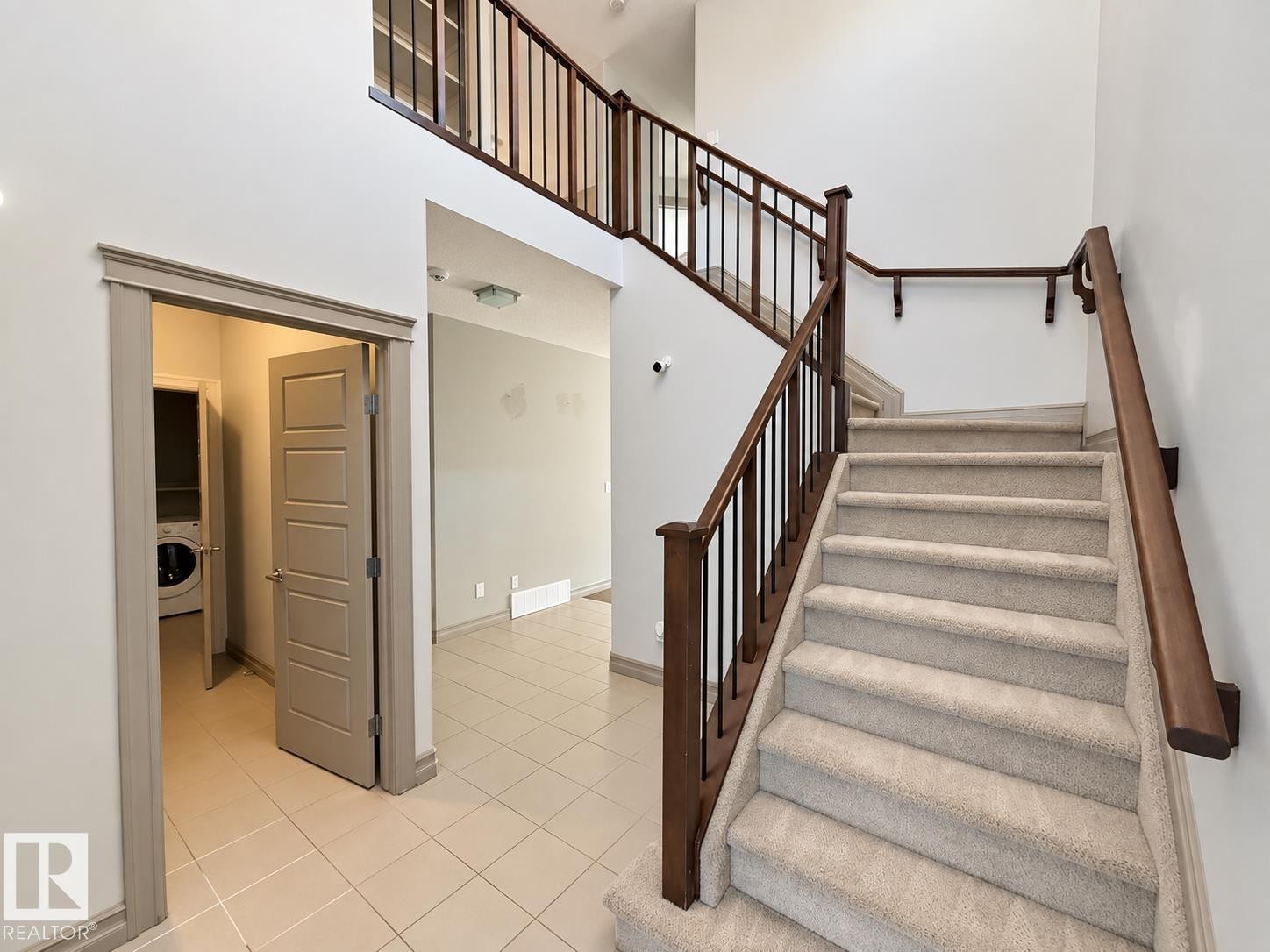 Two-story foyer with a carpeted staircase featuring dark wood newel posts and railings with black metal balusters - 885 Windermere Wynd Nw, Edmonton, AB