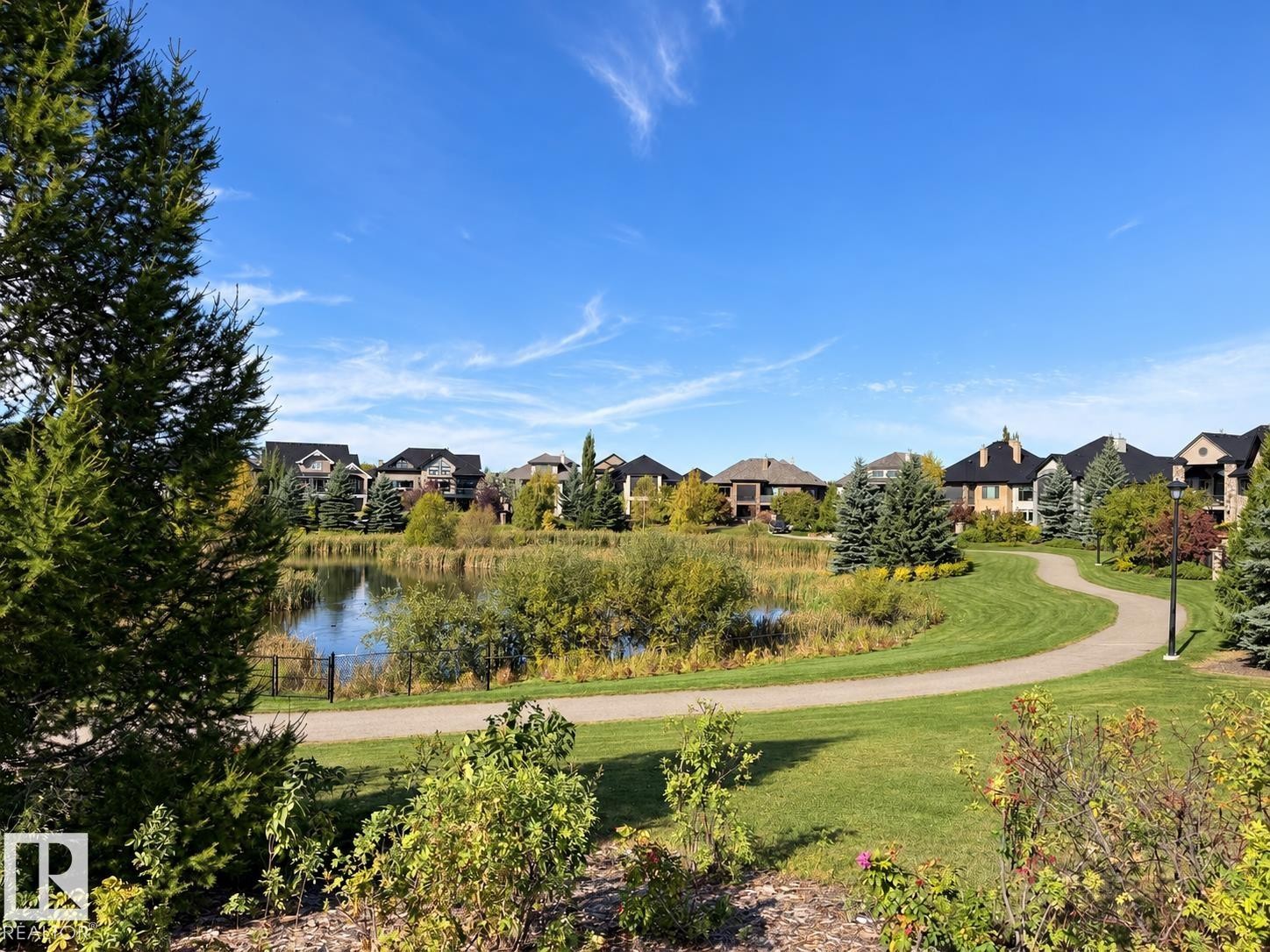 Lush green landscaping with a winding pathway, a serene pond with natural vegetation, and a backdrop of residential properties - 885 Windermere Wynd Nw, Edmonton, AB