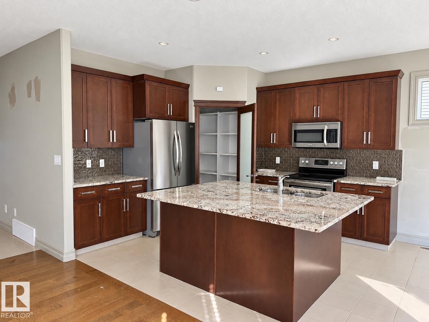 Kitchen featuring a central island with a stone-finish countertop, wood-finish cabinetry, stainless steel appliances, and a pantry with built-in shelving - 885 Windermere Wynd Nw, Edmonton, AB