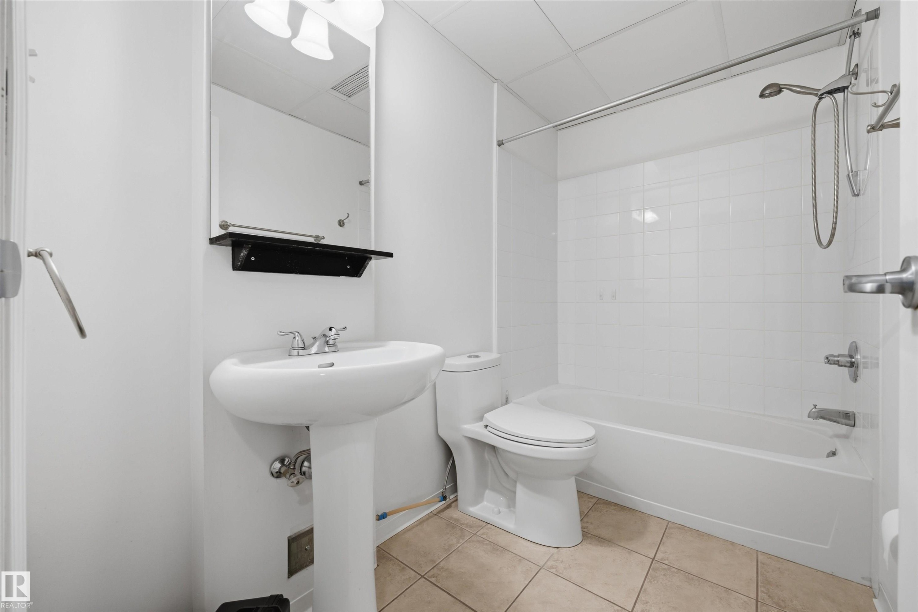 Pedestal sink with chrome faucet, wall-mounted mirror, ceramic tile flooring, shower-over-tub combination with white tile surround, and overhead lighting - #1313 10024 Jasper Av Nw, Edmonton, AB