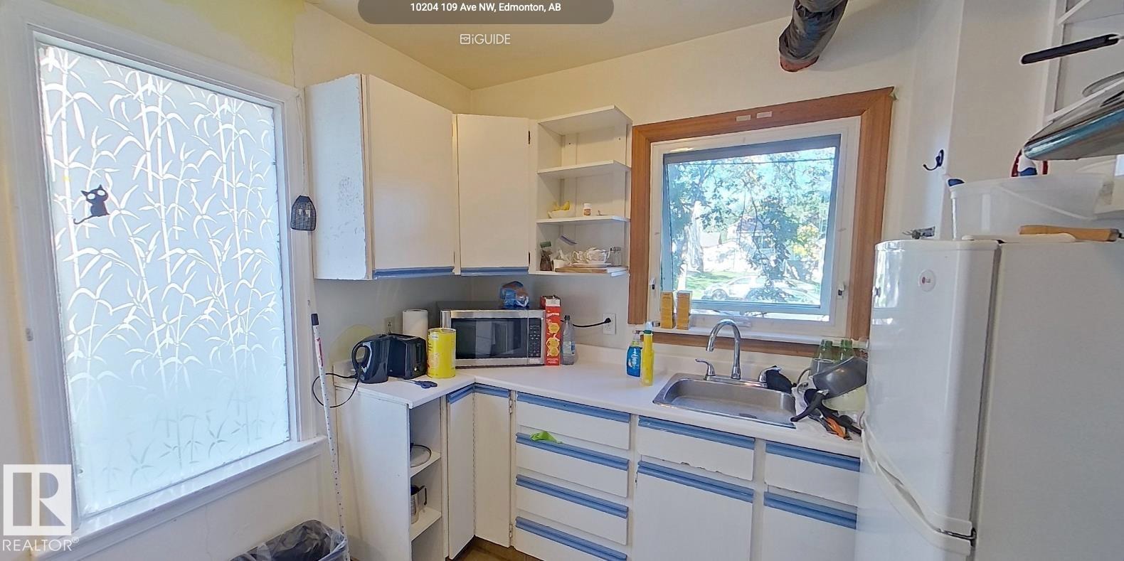 Corner kitchen with white cabinetry, stainless steel sink, and wood-framed window - 10204 123 Avenue Nw, Edmonton, AB