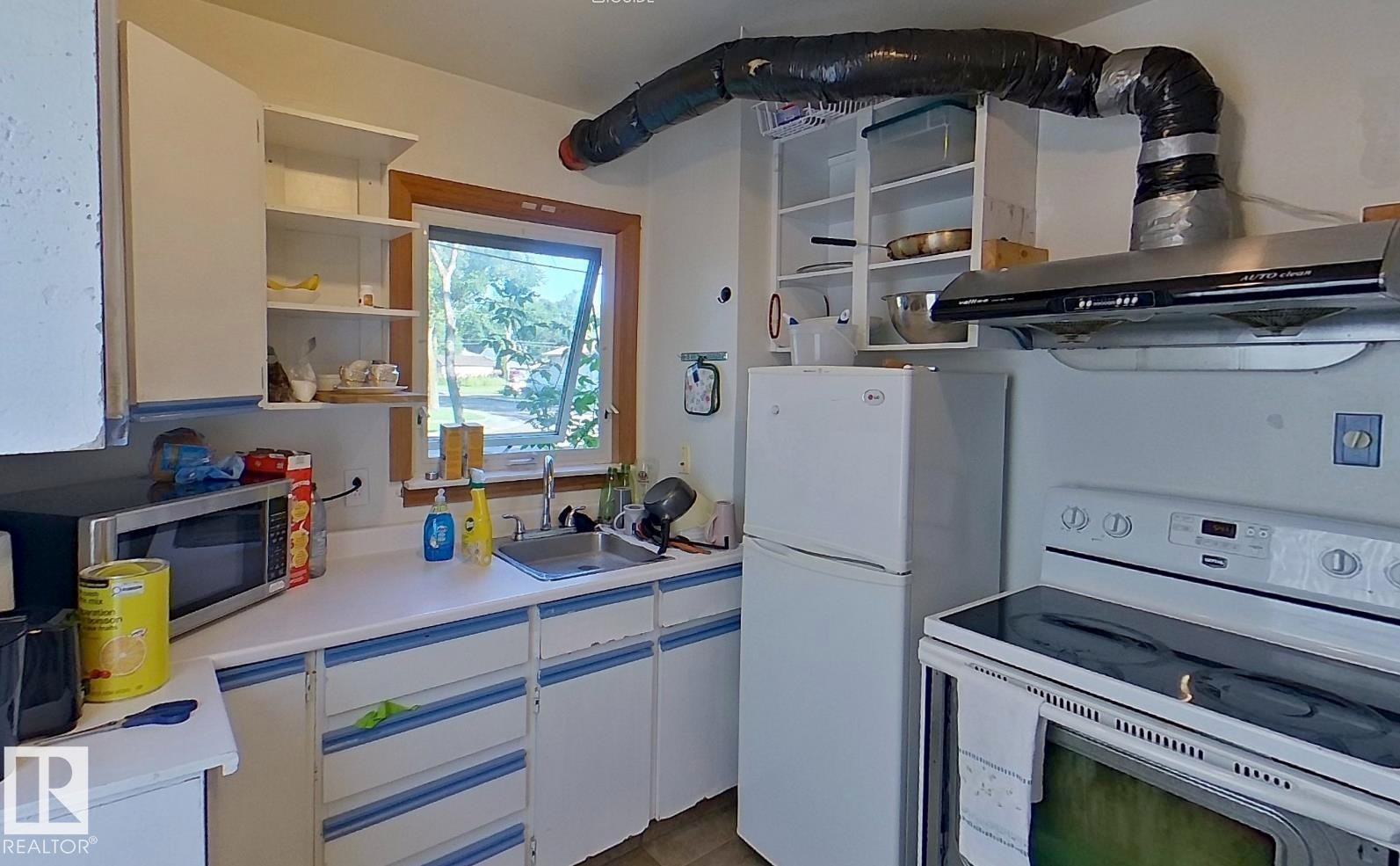 White cabinetry with blue trim, countertop space, kitchen sink, wall-mounted shelving, and window - 10204 123 Avenue Nw, Edmonton, AB