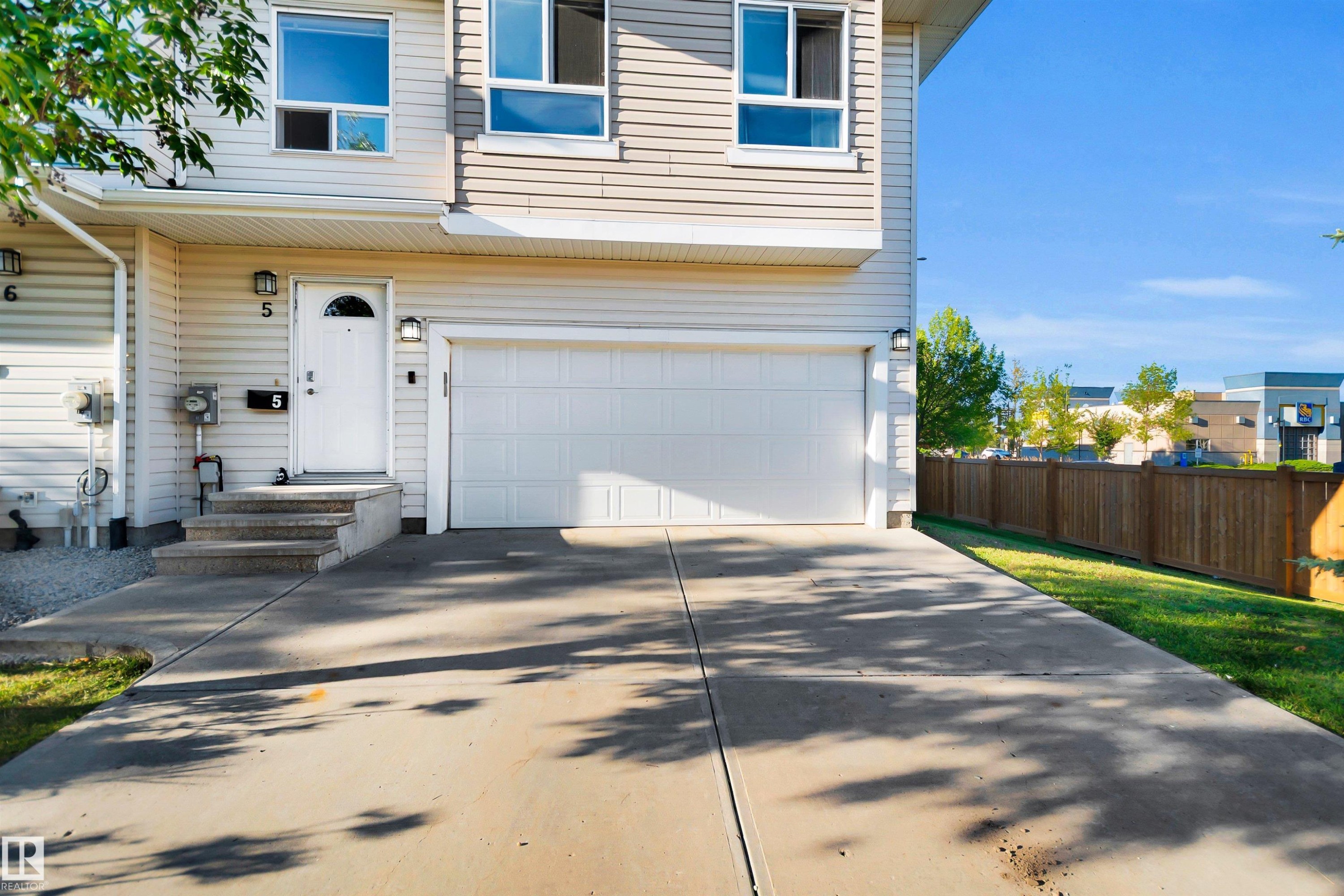 Cream-colored siding exterior, attached garage with a white door, concrete driveway, front entrance with concrete steps, and a wooden privacy fence - #5 5120 164 Av Nw, Edmonton, AB