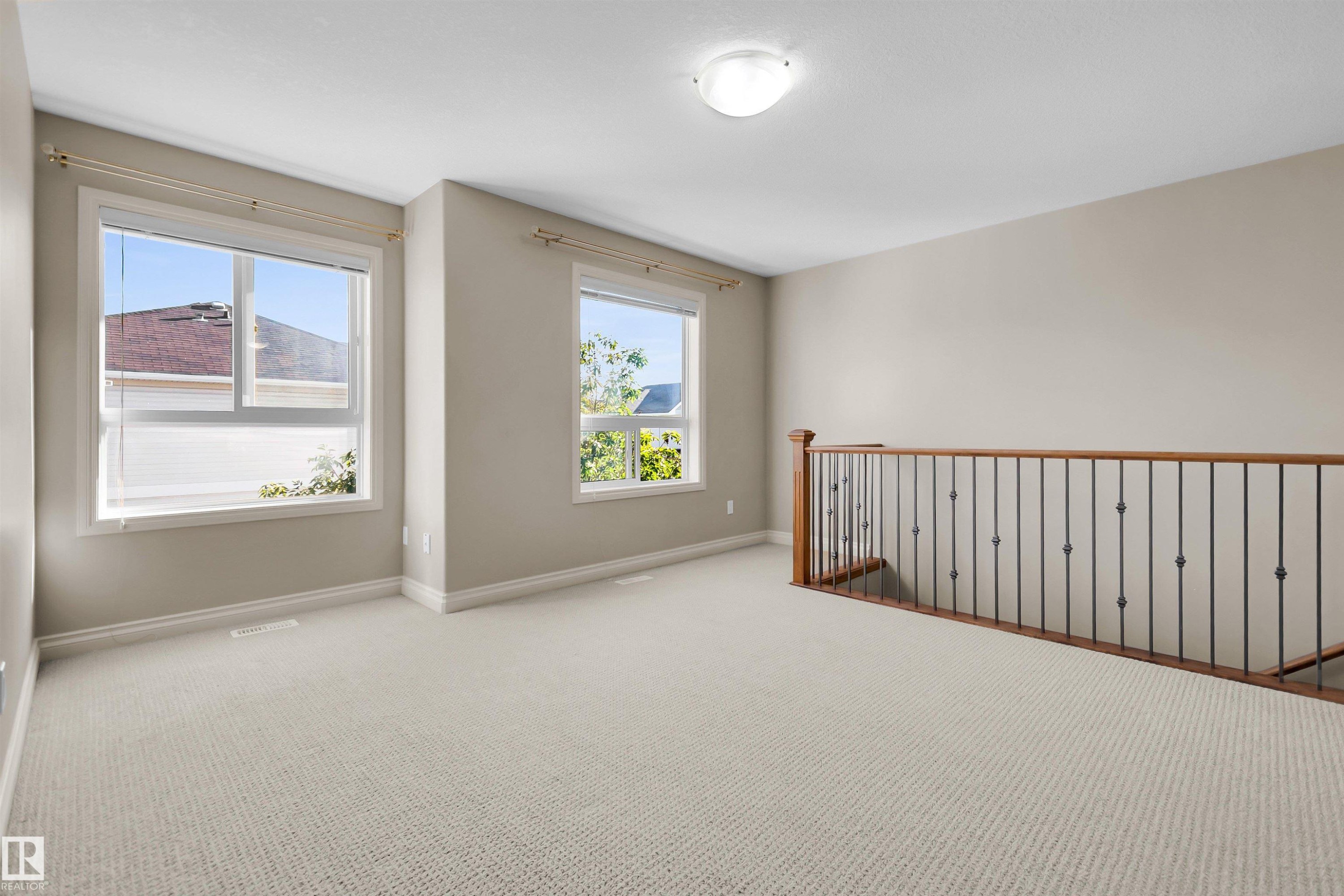 Carpeted open area with two windows, a light fixture, and a wood and wrought iron staircase railing - #5 5120 164 Av Nw, Edmonton, AB