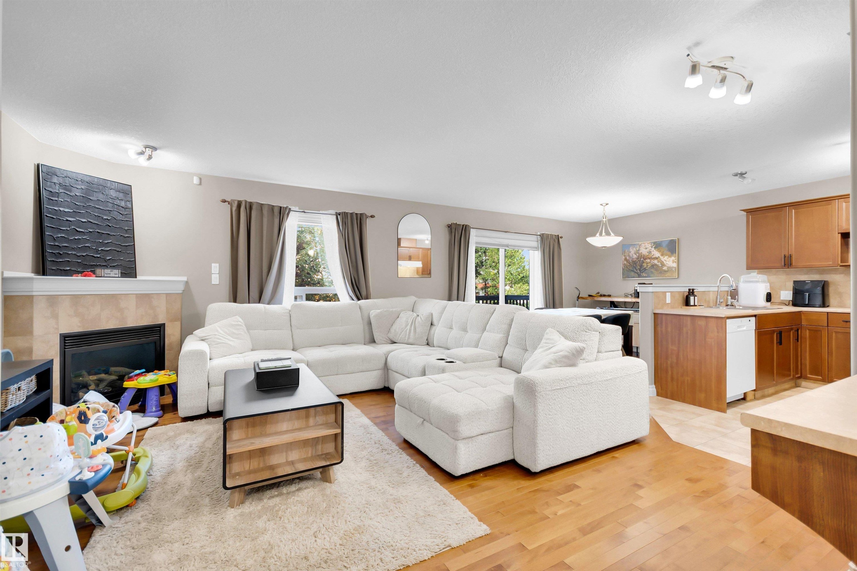 Living area featuring a gas fireplace with a tile surround, wood-finish flooring, and a kitchen with wood cabinetry and a dishwasher - #5 5120 164 Av Nw, Edmonton, AB