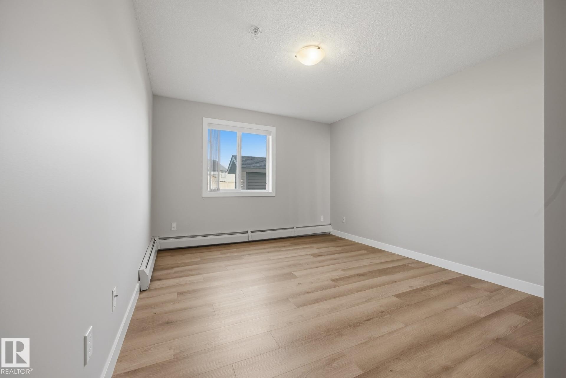 Neutral gray walls, wood-finish flooring, white window trim, and a ceiling-mounted light fixture - #122 240 Spruce Ridge Rd, Spruce Grove, AB