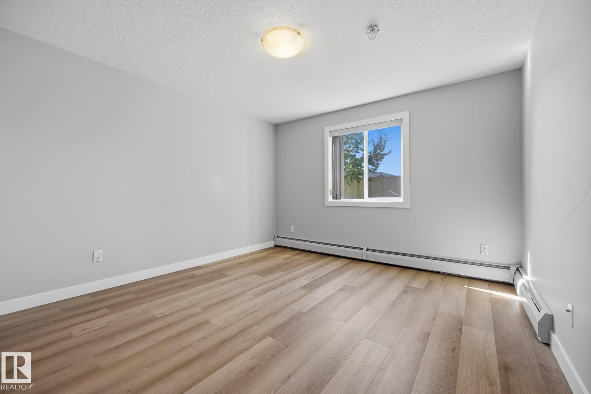 Bright room featuring wood-finish flooring, light grey walls, white trim, and a window with white casing - #122 240 Spruce Ridge Rd, Spruce Grove, AB