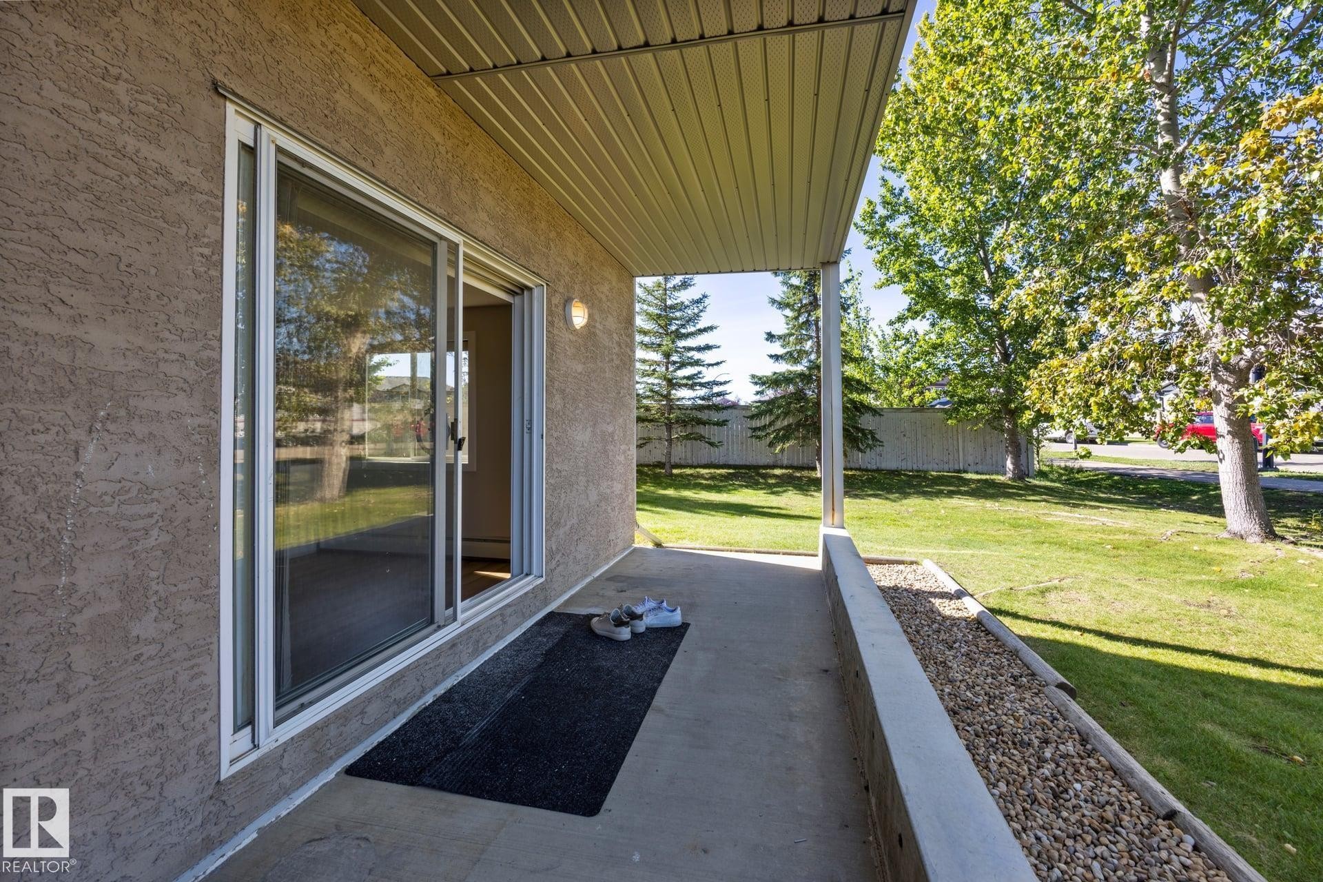 Covered patio with textured stucco exterior, sliding glass door, and integrated wall sconce lighting - #122 240 Spruce Ridge Rd, Spruce Grove, AB