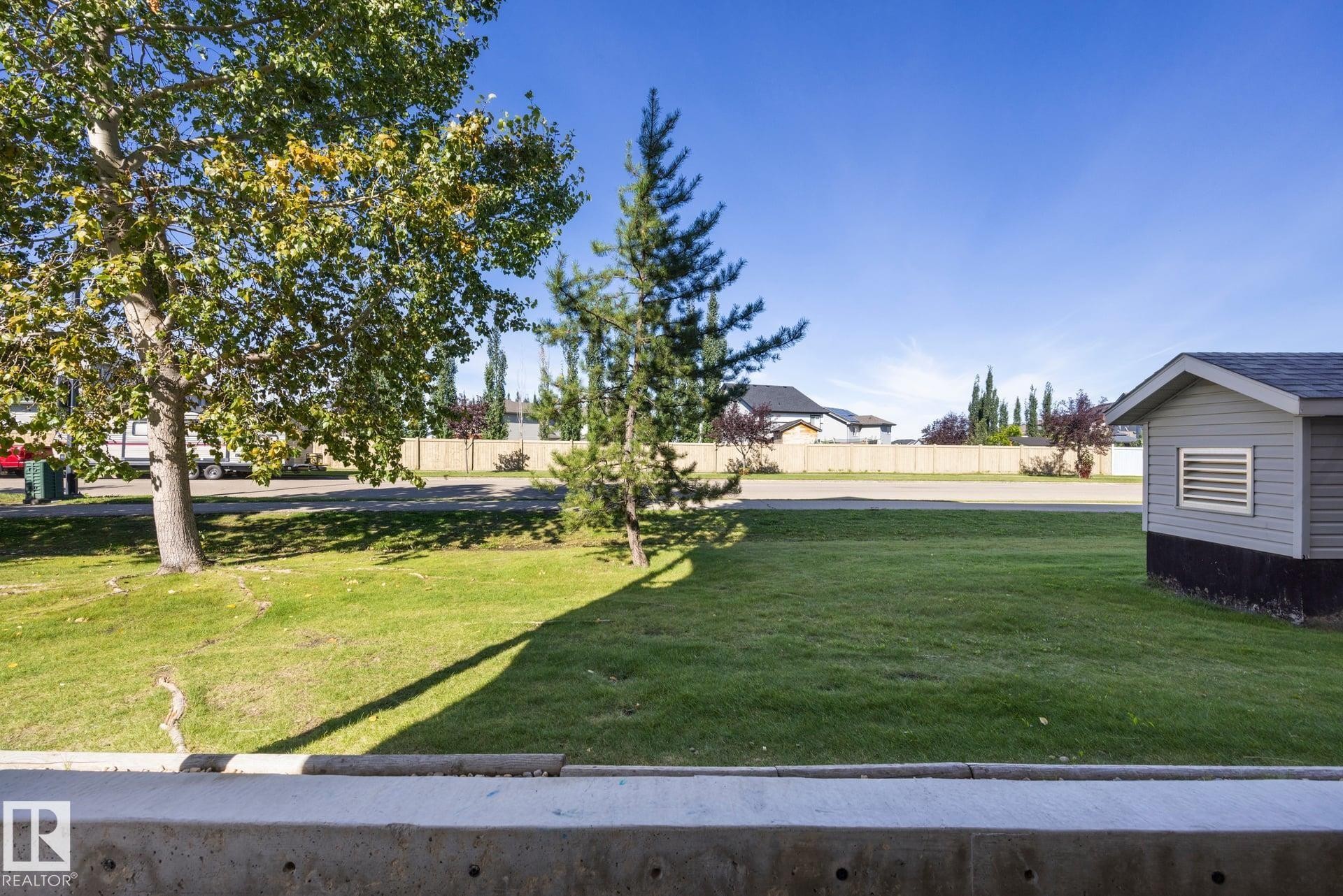 Manicured lawn with mature trees and a detached shed featuring horizontal siding and a shingled roof - #122 240 Spruce Ridge Rd, Spruce Grove, AB