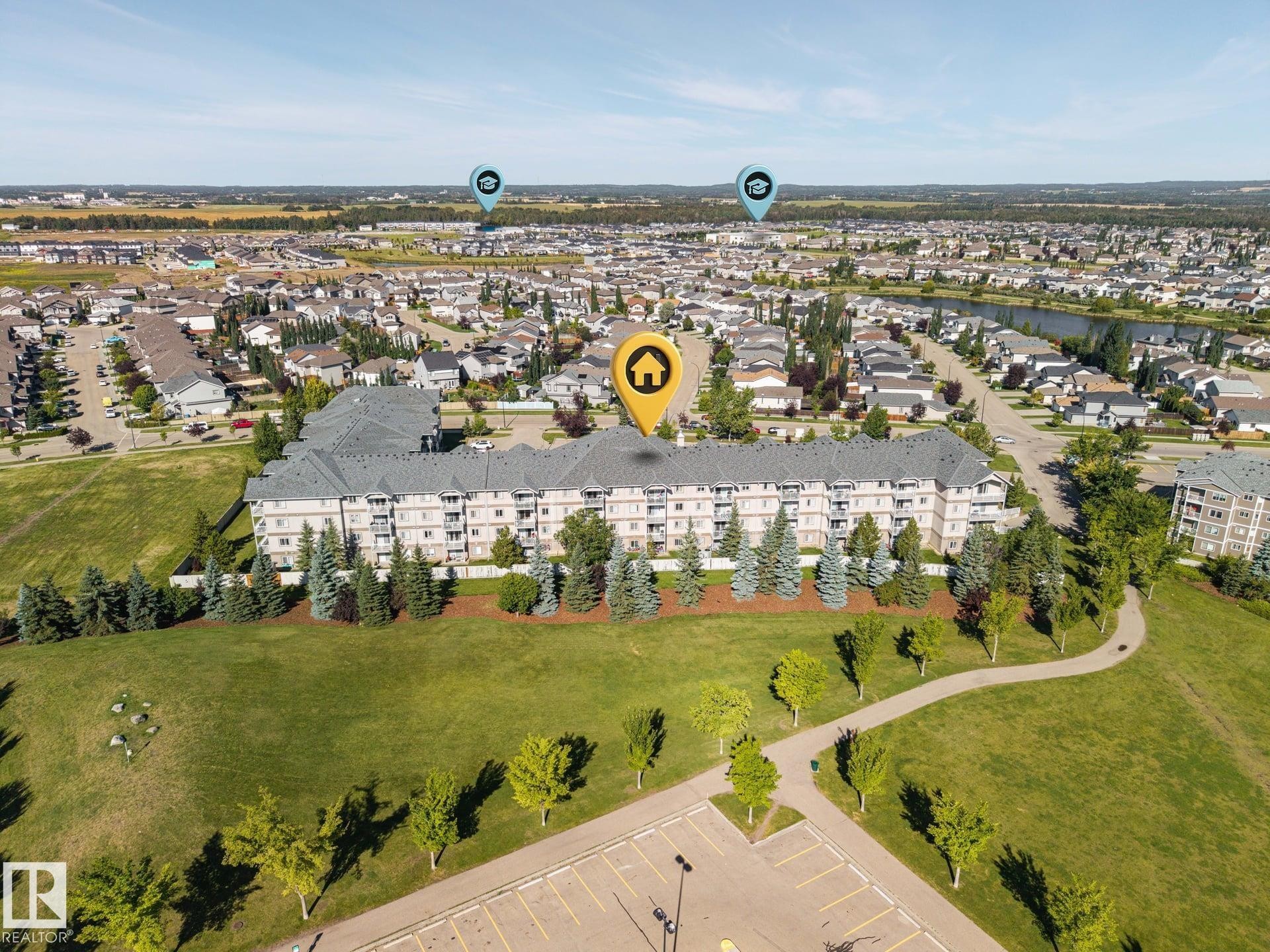 Multi-story residential building with balconies, surrounded by mature trees and manicured green space - #122 240 Spruce Ridge Rd, Spruce Grove, AB