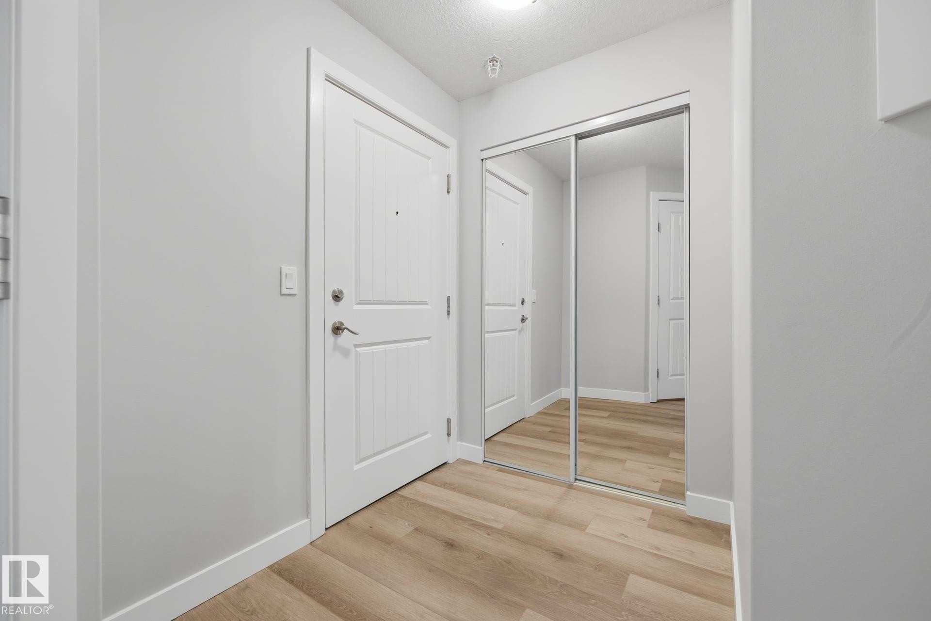 Entryway featuring wood-finish flooring, white paneled doors, and mirrored sliding closet doors - #122 240 Spruce Ridge Rd, Spruce Grove, AB
