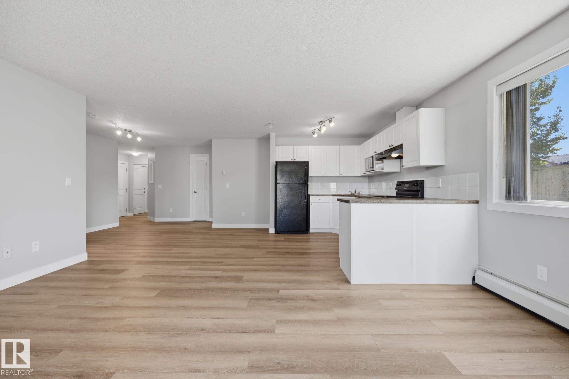 Open-concept living area featuring wood-finish flooring, white cabinetry, track lighting, and a kitchen island with a countertop - #122 240 Spruce Ridge Rd, Spruce Grove, AB