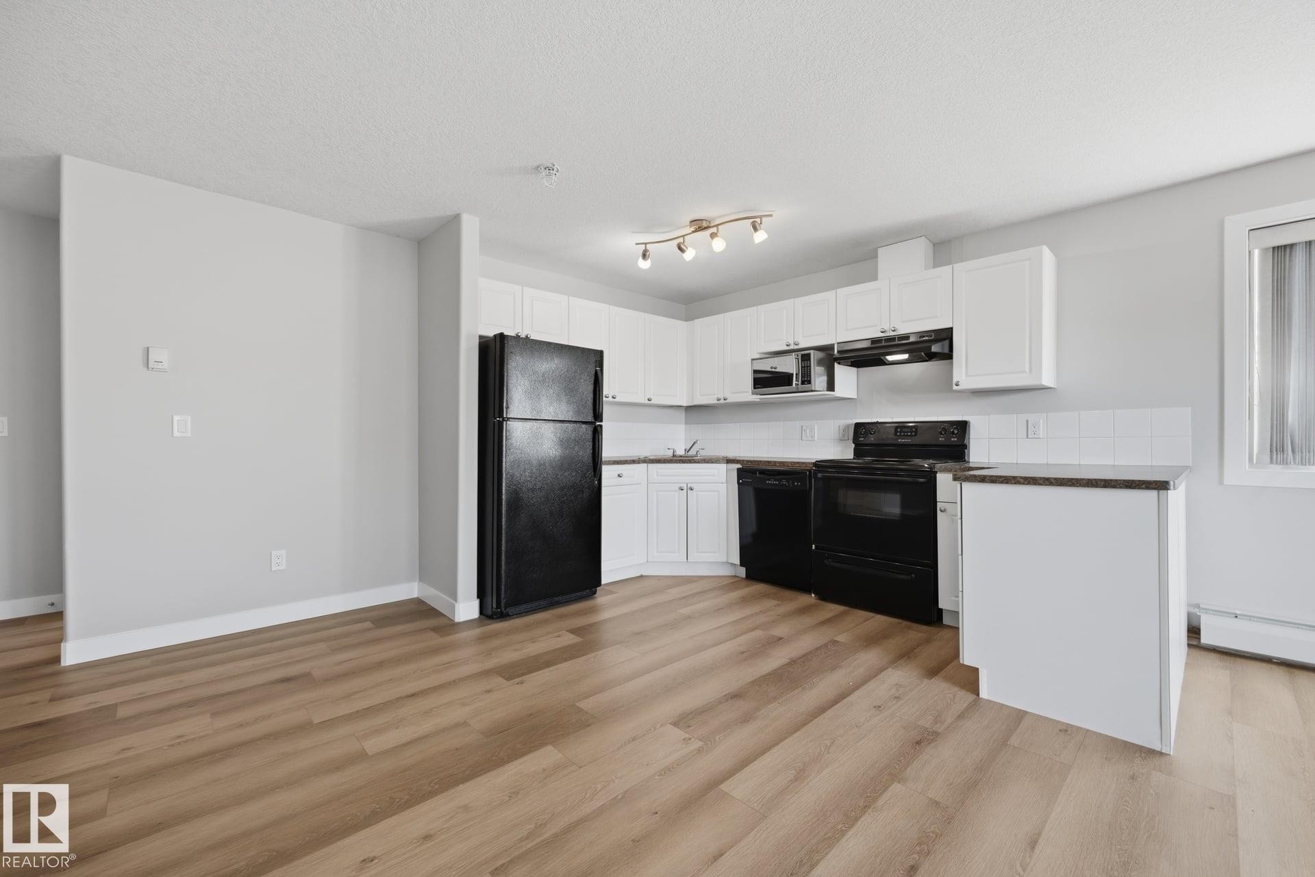 Wood-finish flooring, white cabinetry, dark countertops, white tile backsplash, and track lighting fixture - #122 240 Spruce Ridge Rd, Spruce Grove, AB