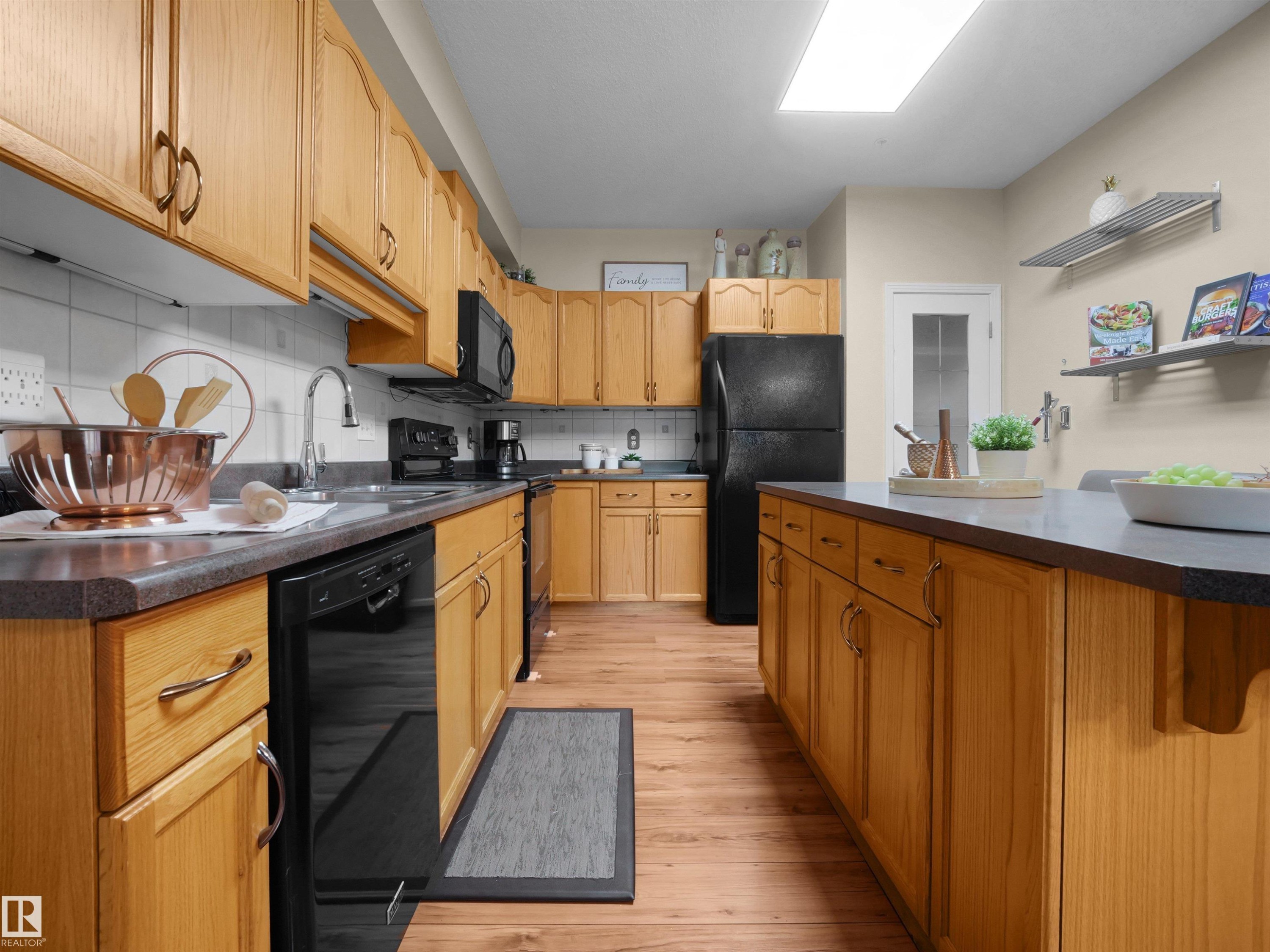Wood-finish flooring, a kitchen island with built-in cabinetry, and black appliances - #206 12111 51 Av Nw, Edmonton, AB