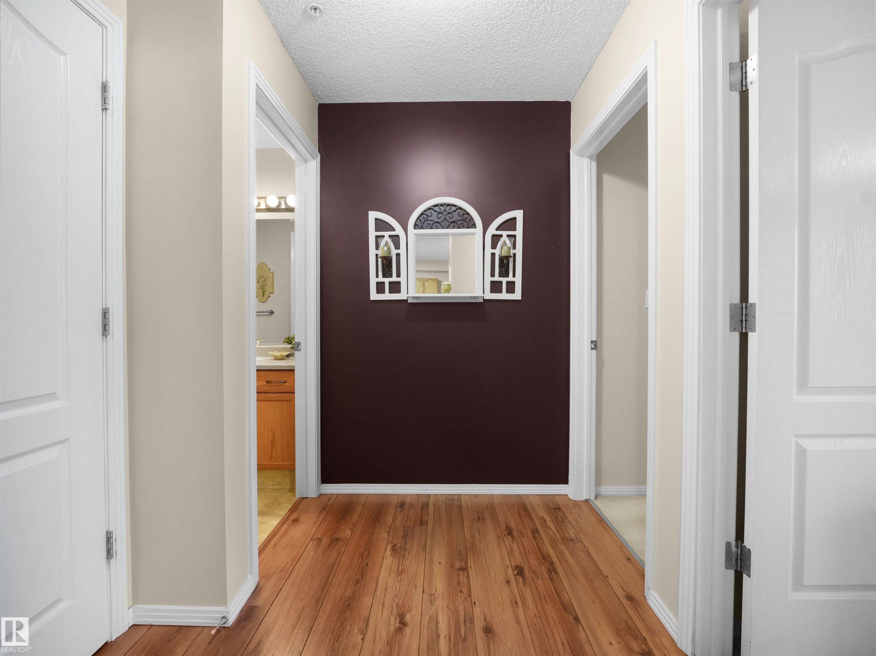 Hallway featuring warm wood-finish flooring, soft neutral wall finishes, and multiple white panel doors - #206 12111 51 Av Nw, Edmonton, AB