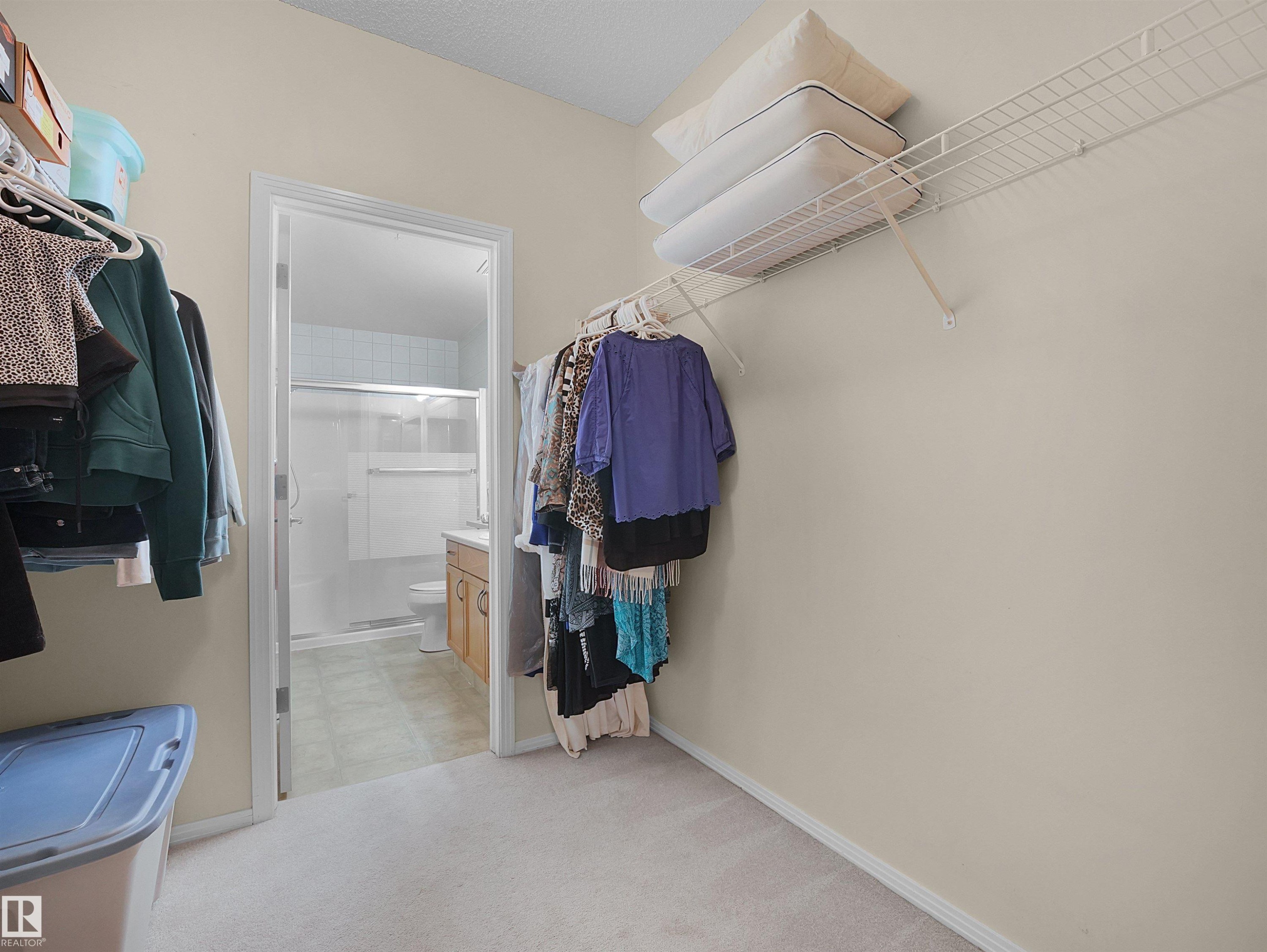 Carpeted walk-in closet featuring wire shelving and direct access to a full bathroom - #206 12111 51 Av Nw, Edmonton, AB