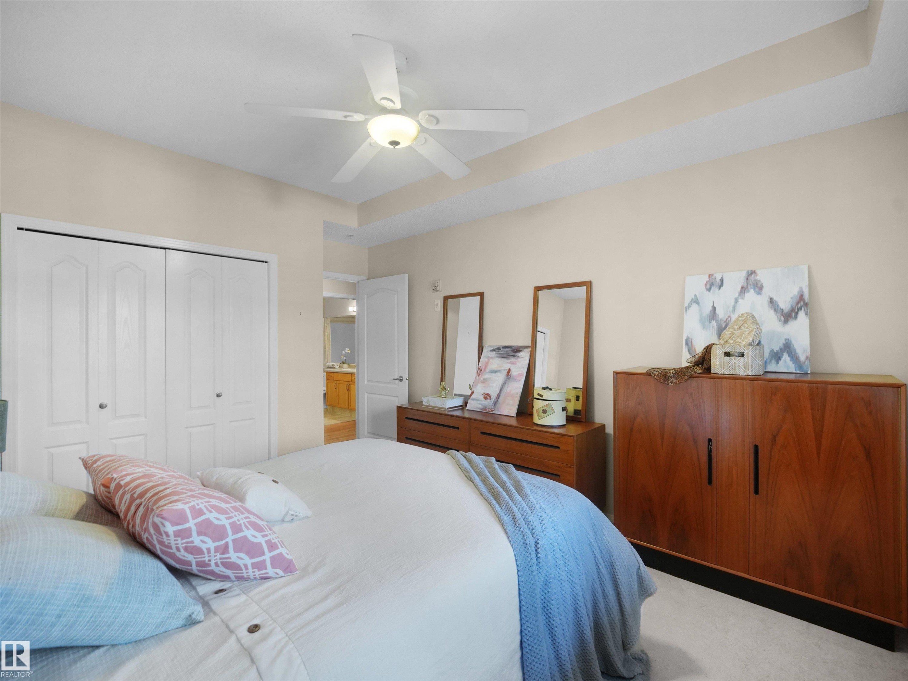 Recessed tray ceiling with a ceiling fan, bi-fold closet doors, and light-colored carpeting - #206 12111 51 Av Nw, Edmonton, AB