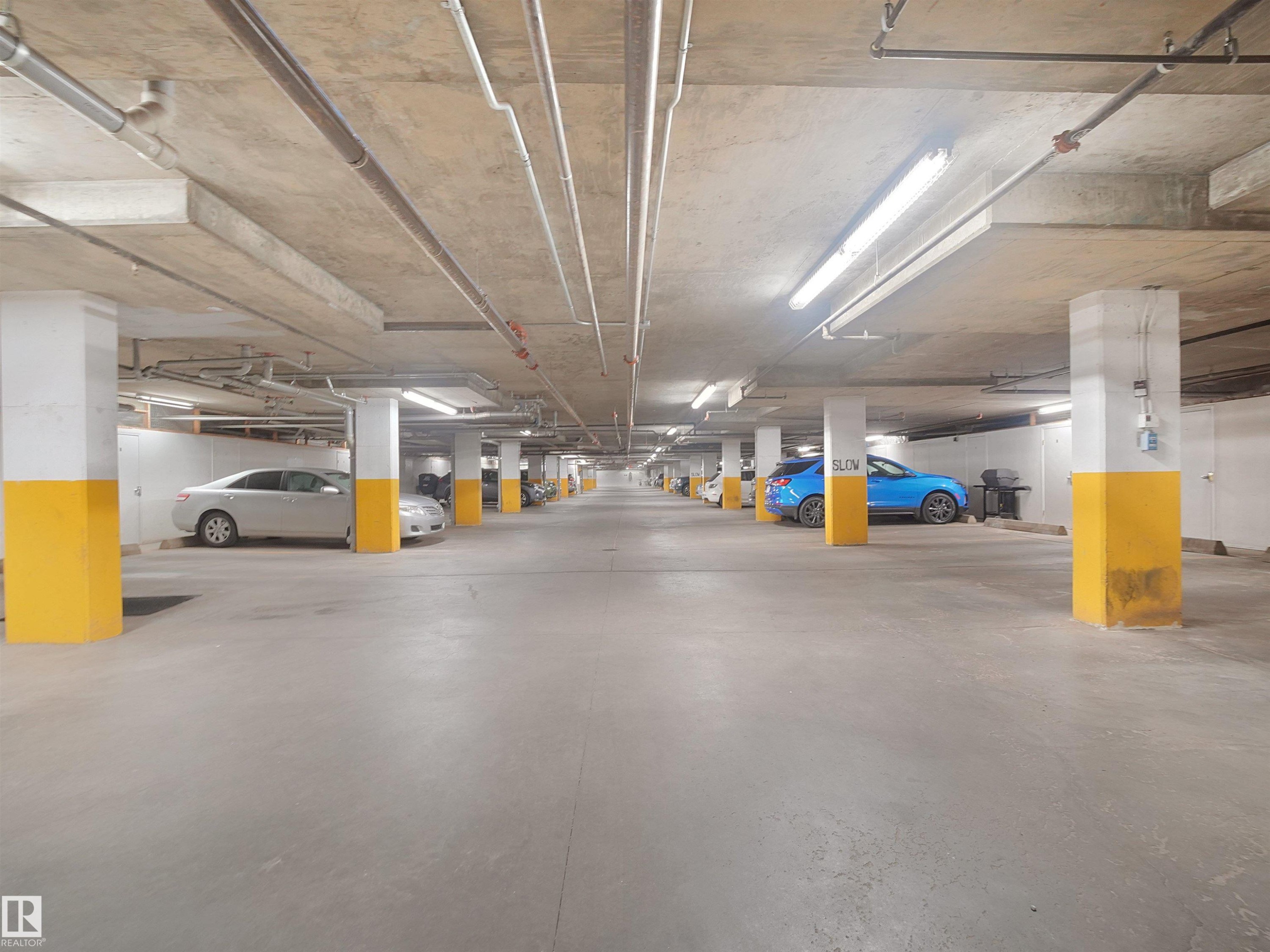 Underground parking facility with concrete flooring, structural columns, and overhead lighting - #206 12111 51 Av Nw, Edmonton, AB