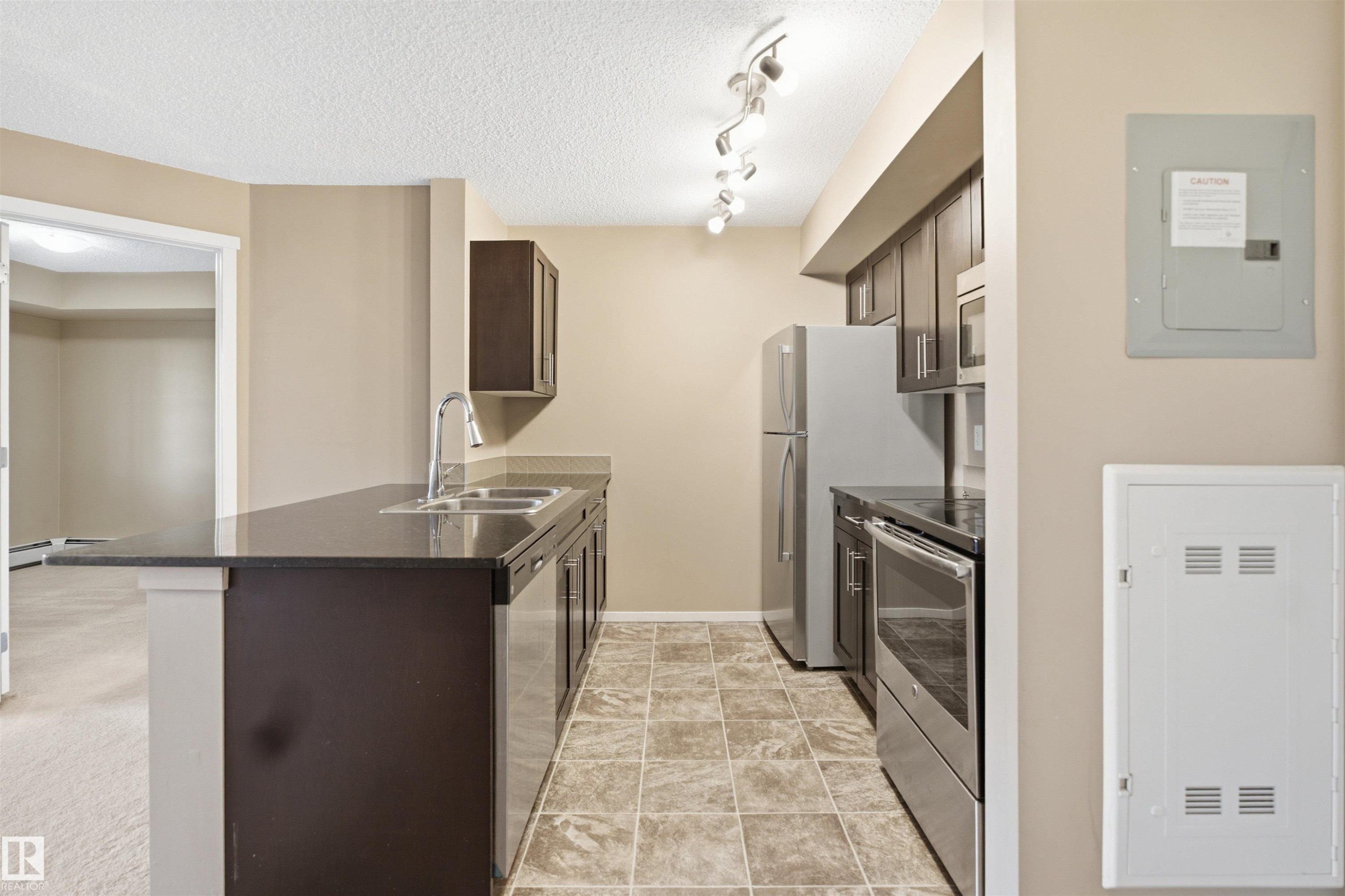Kitchen featuring dark cabinetry, stainless steel appliances, track lighting, and a double basin sink - #225 1510 Watt Dr Sw, Edmonton, AB