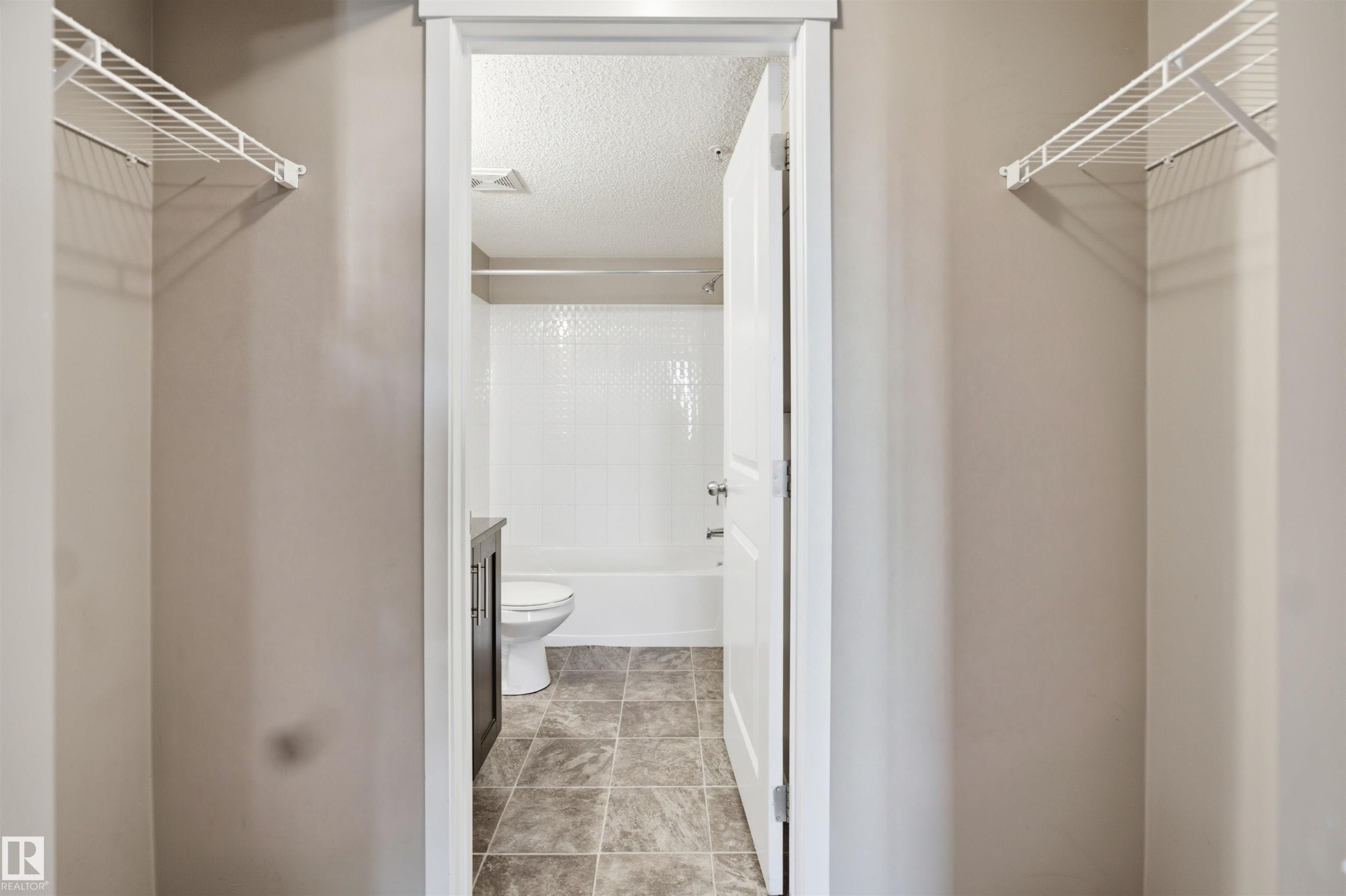 Bathroom featuring a white bathtub with tile surround, a toilet, and a dark wood-finish vanity - #225 1510 Watt Dr Sw, Edmonton, AB