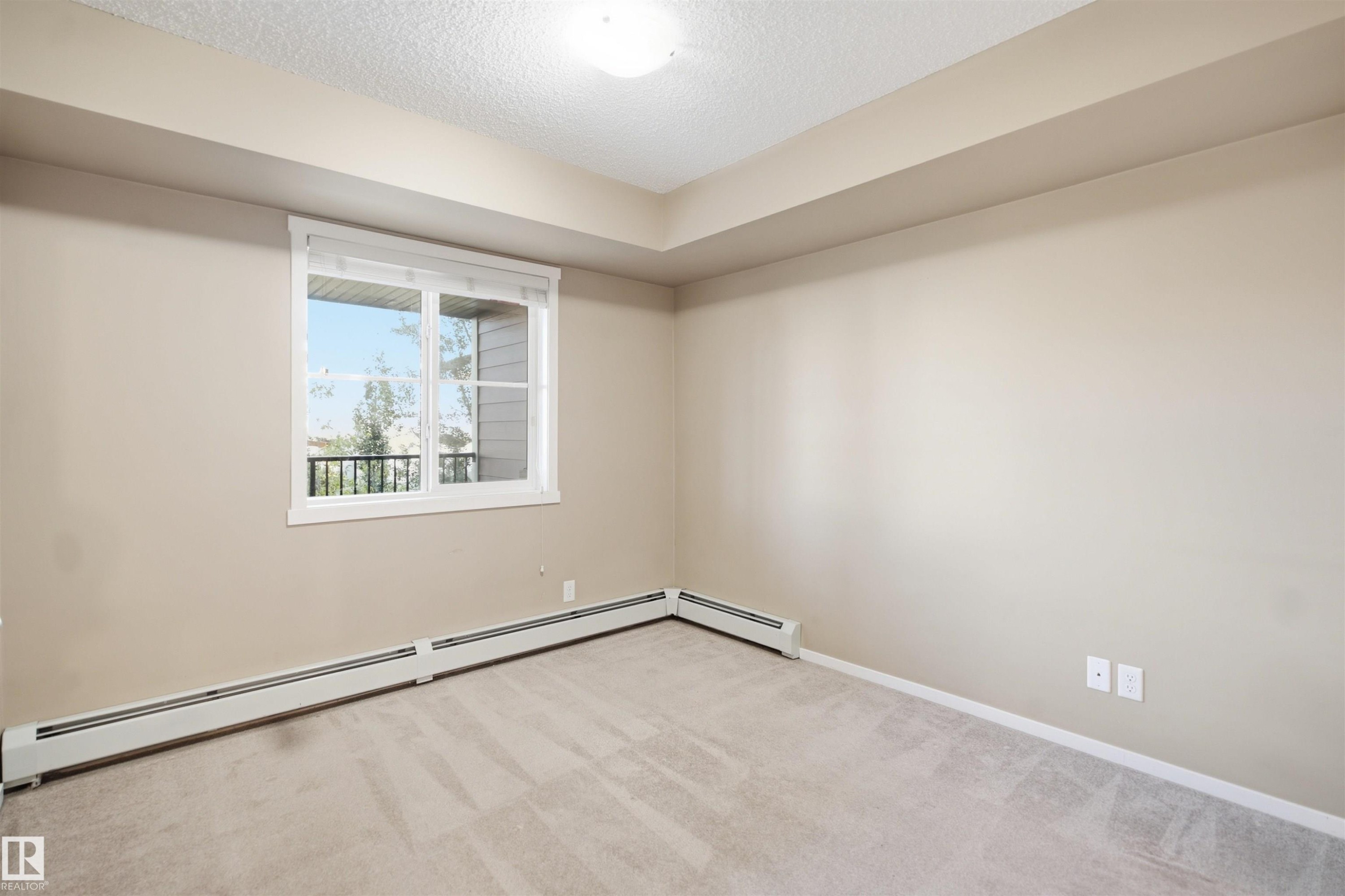Carpeted room featuring a white-framed window, neutral painted walls, and overhead lighting - #225 1510 Watt Dr Sw, Edmonton, AB