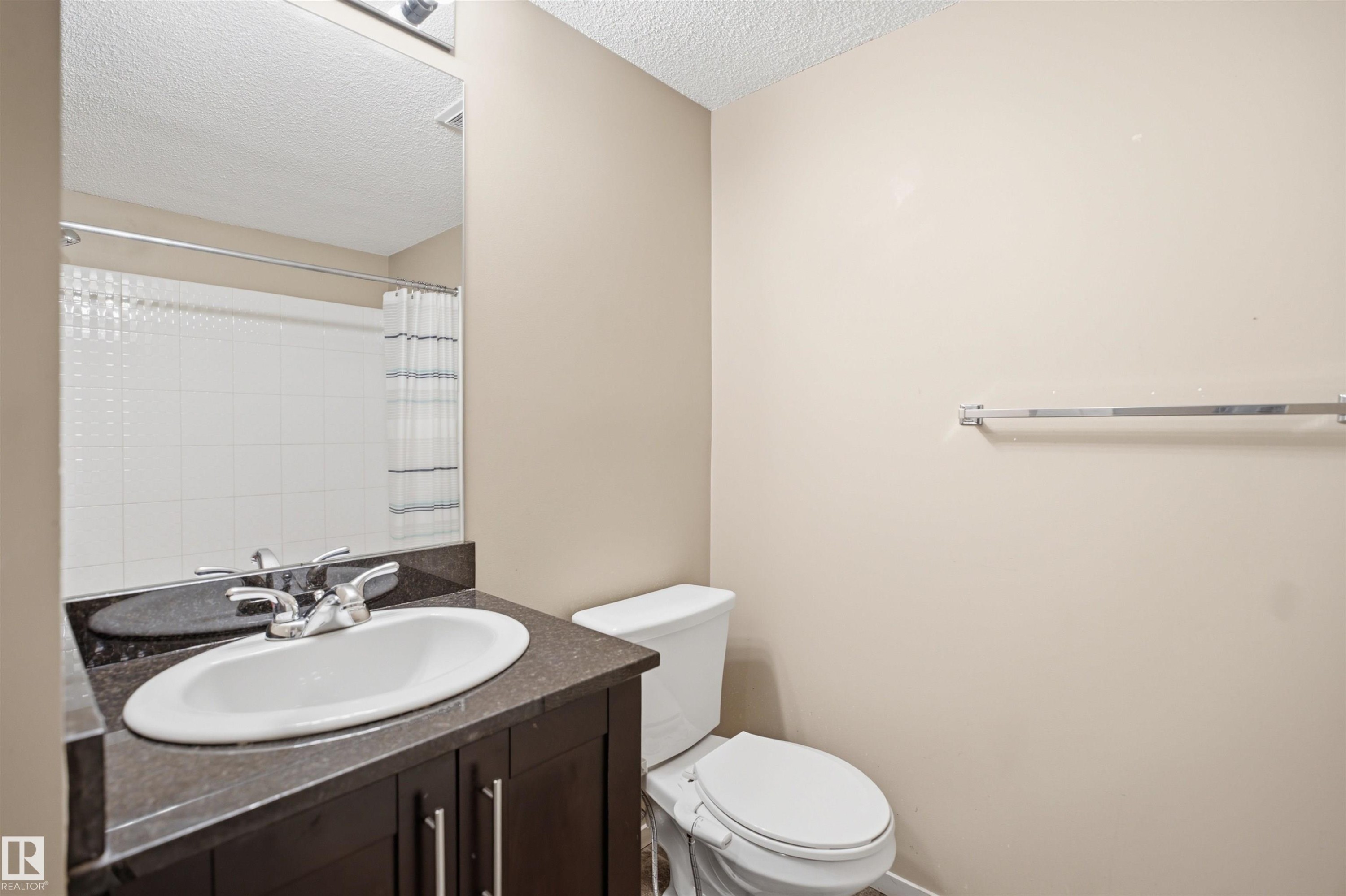 Vanity with integrated sink, dark wood-finish cabinetry, and stone-look countertop - #225 1510 Watt Dr Sw, Edmonton, AB