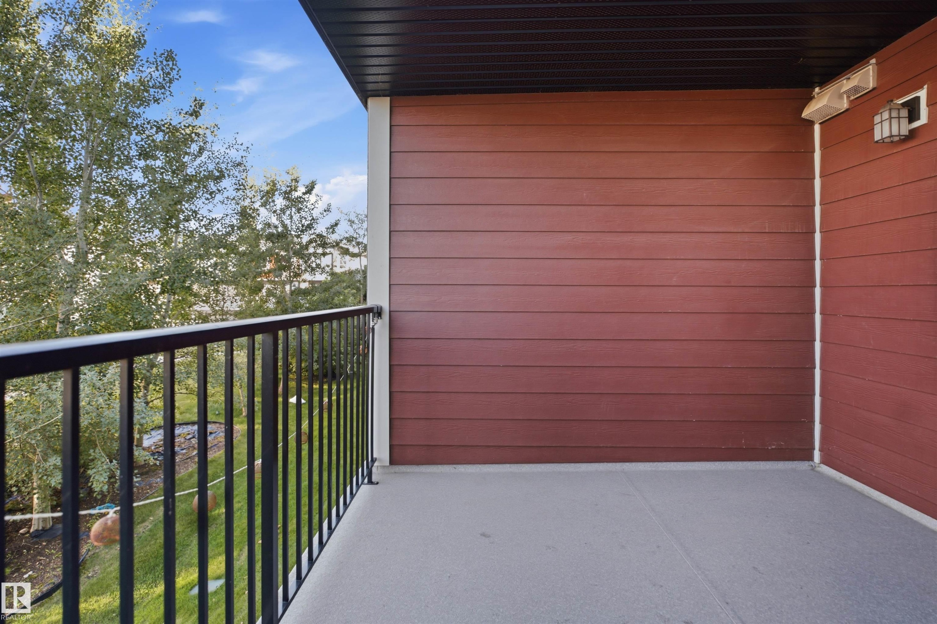 Outdoor balcony with a smooth concrete surface, dark metal railing, and red horizontal siding - #225 1510 Watt Dr Sw, Edmonton, AB