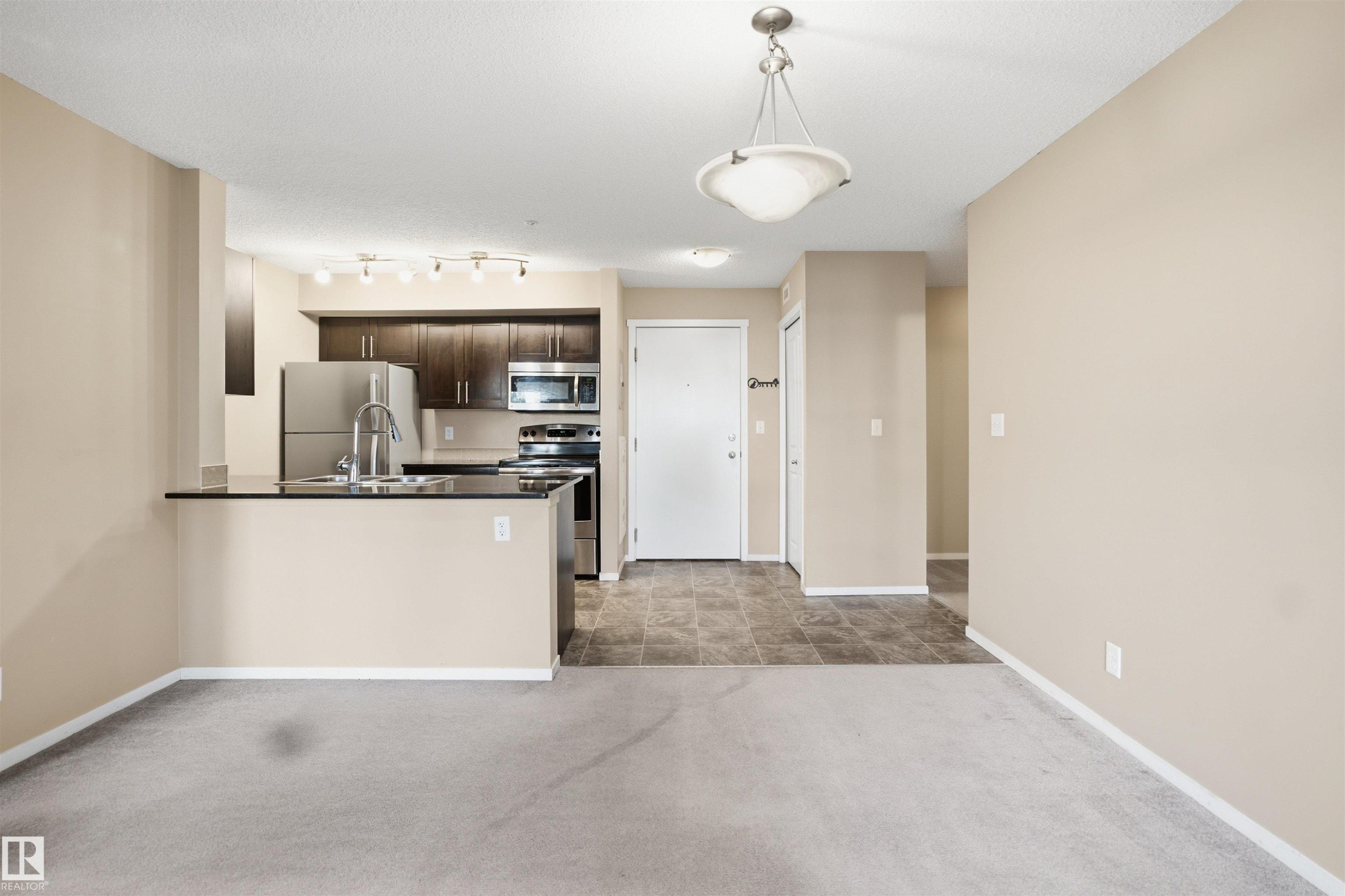 Kitchen featuring dark wood-finish cabinetry, stainless steel appliances, and a breakfast bar - #225 1510 Watt Dr Sw, Edmonton, AB