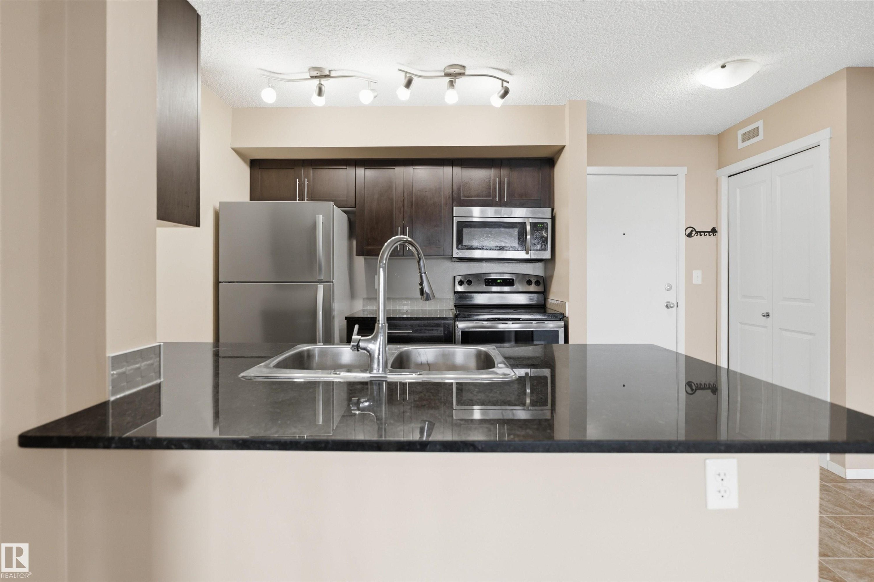 Kitchen featuring a double basin stainless steel sink, dark cabinetry, and stainless steel appliances - #225 1510 Watt Dr Sw, Edmonton, AB