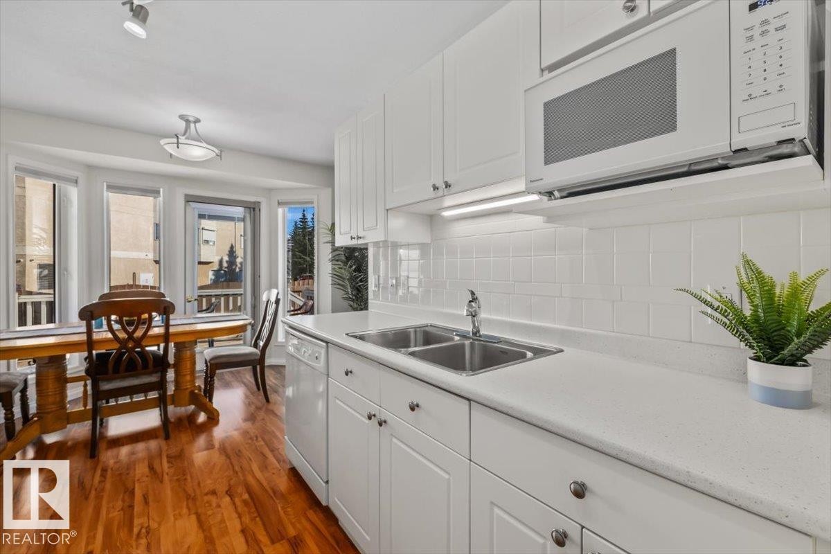 White cabinetry, light-colored countertops, dual basin sink, white tile backsplash, and wood-finish flooring - #92 13320 124 St Nw, Edmonton, AB
