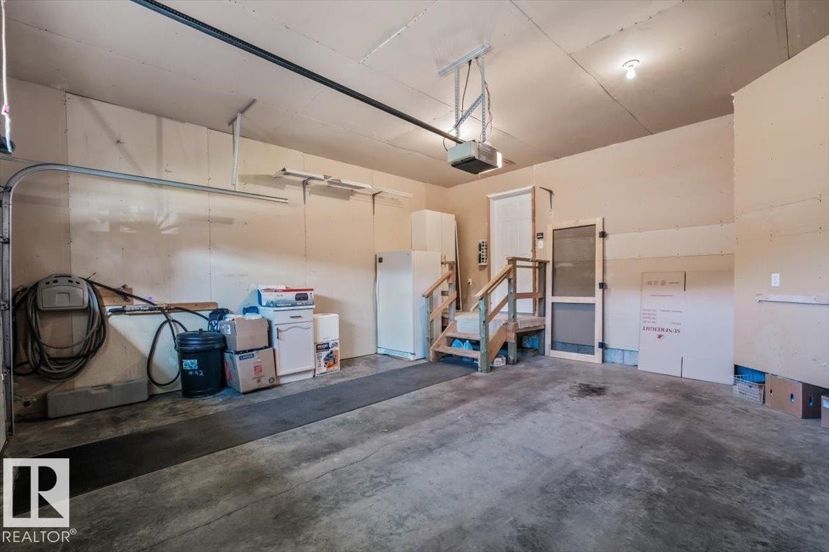 Attached garage with a concrete floor, automatic garage door opener, and interior access via a wooden staircase - #92 13320 124 St Nw, Edmonton, AB