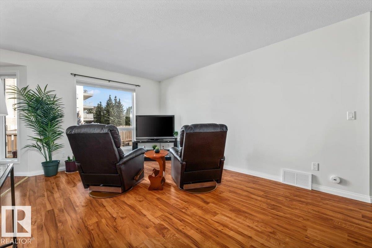 Spacious living area featuring wood-finish flooring, white walls, and an expansive window - #92 13320 124 St Nw, Edmonton, AB