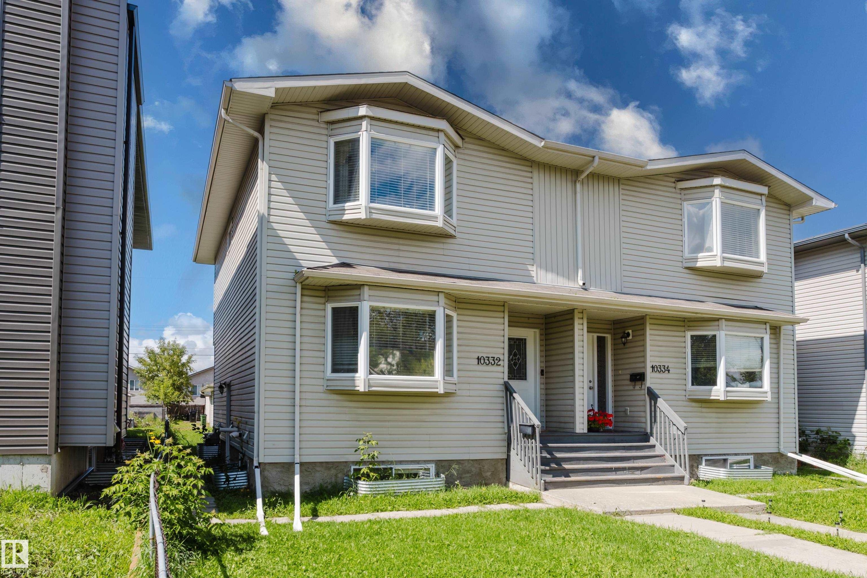 Two-story duplex featuring neutral-toned siding, multiple bay windows, individual front entries, and a grassed front yard - 10332 161 Street Nw, Edmonton, AB