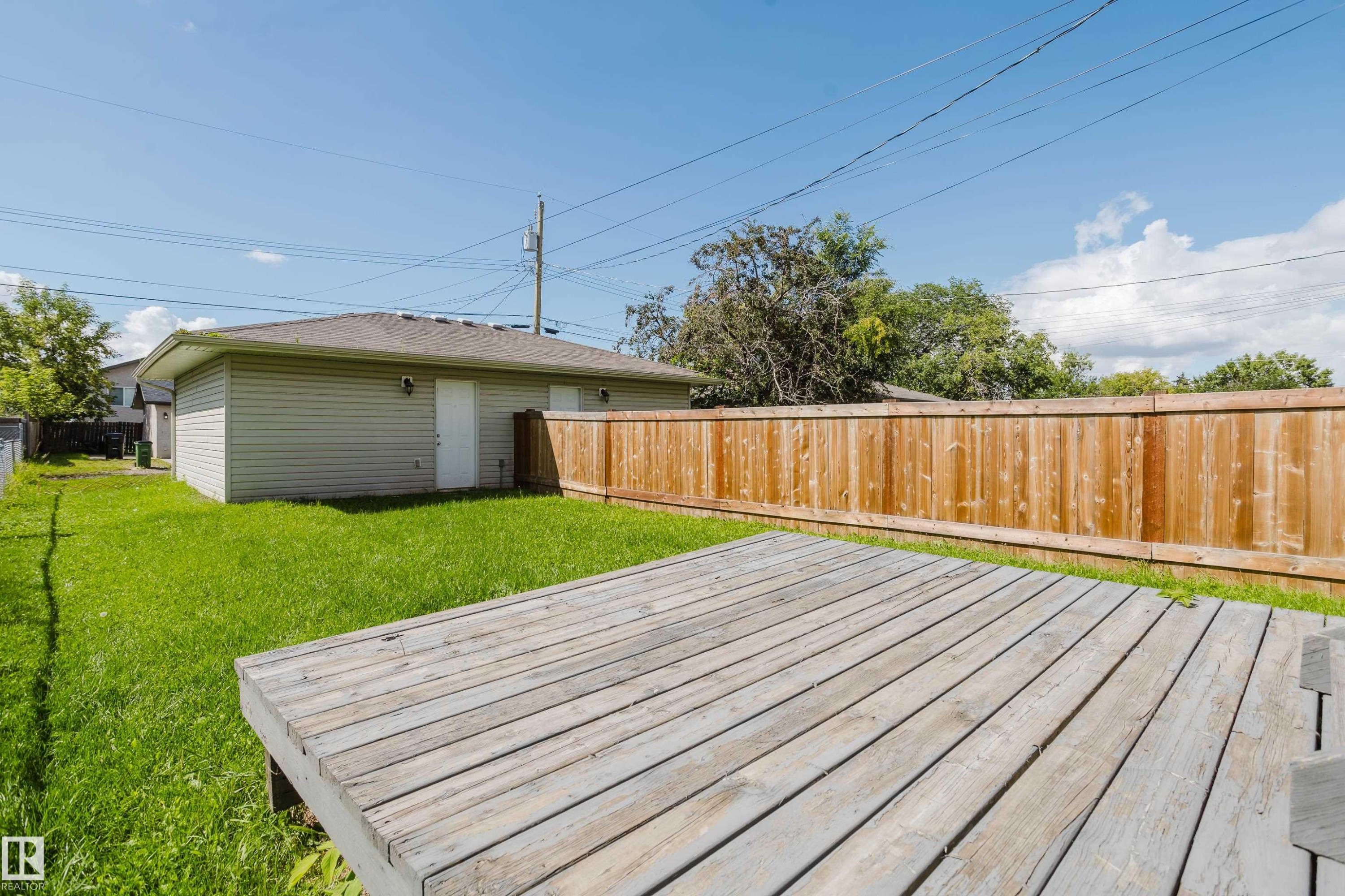 Expansive backyard featuring a wood deck, manicured lawn, and a light wood privacy fence - 10332 161 Street Nw, Edmonton, AB