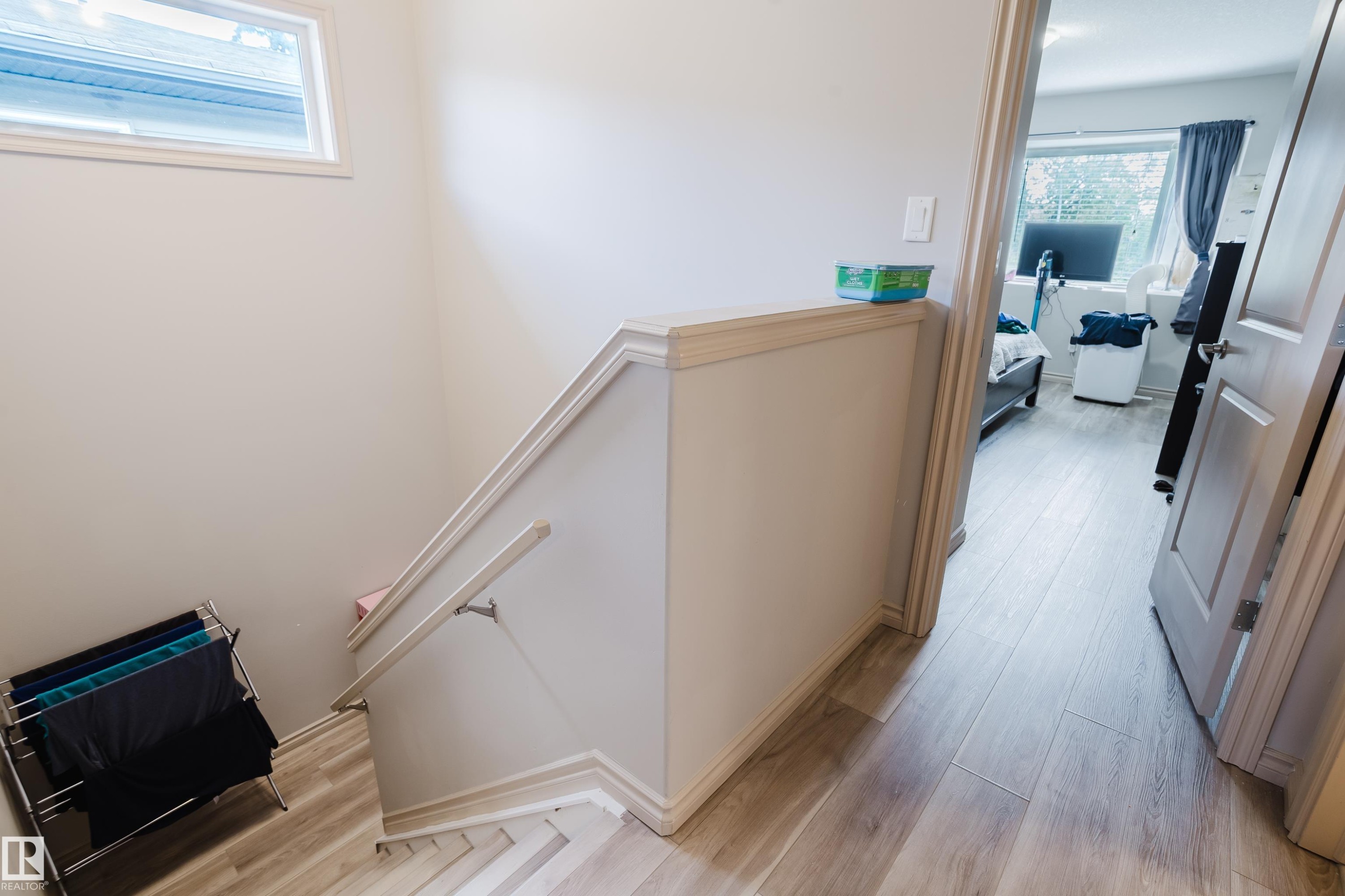 Wood-finish flooring throughout, featuring a staircase with a white painted handrail and a high-set window - 10334 161 Street Nw, Edmonton, AB